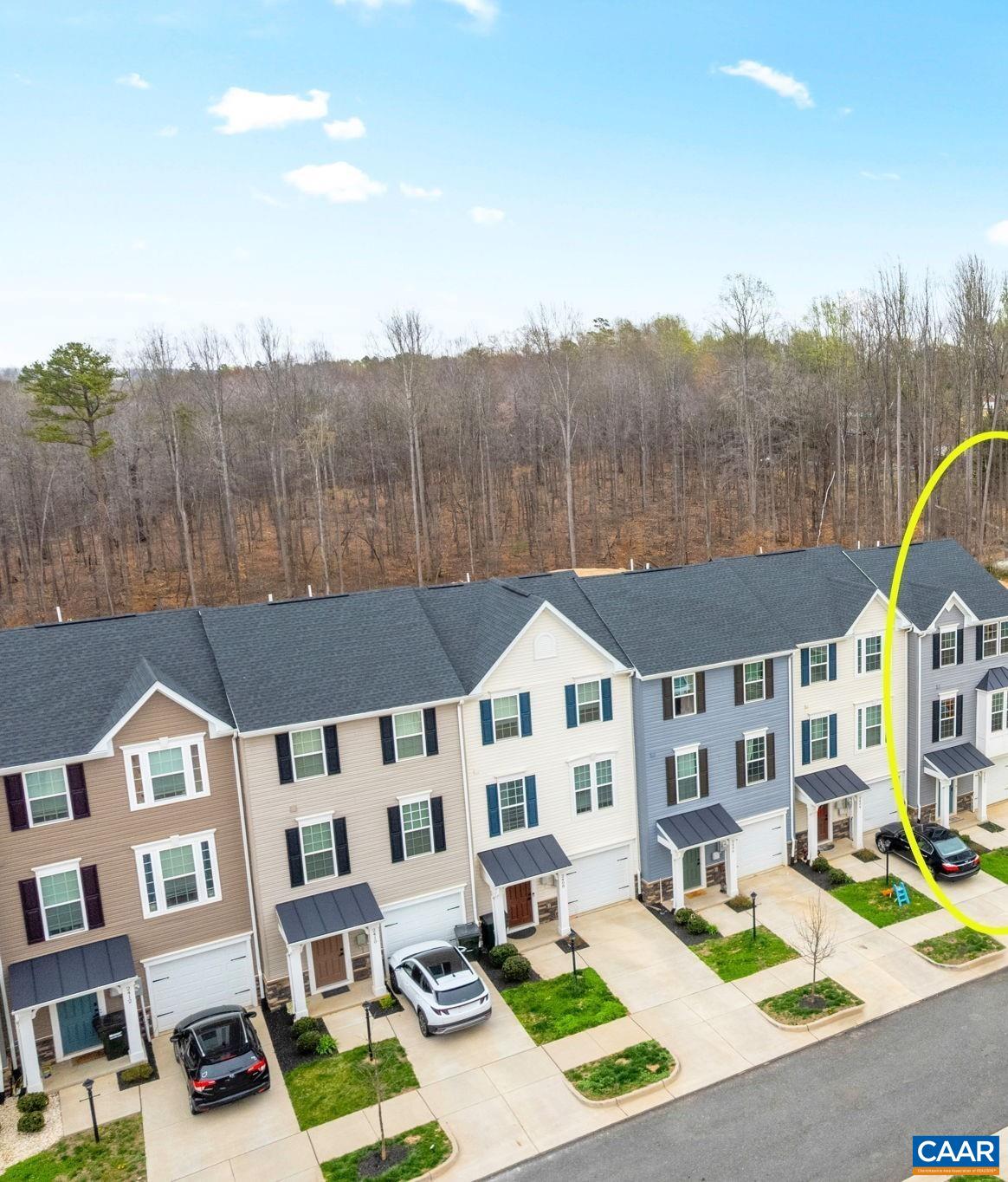 Aerial view of the home highlighting its position within the community, featuring a one-car garage, private driveway, and a row of modern townhomes backing to a wooded area for added privacy. Aerial view of the home highlighting its position within the community, featuring a one-car garage, private driveway, and a row of modern townhomes backing to a wooded area for added privacy.