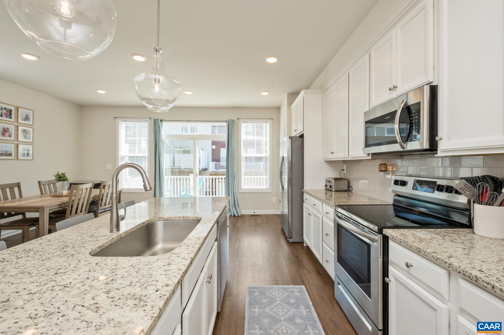 Open kitchen features white cabinets, granite counters and stainless steel appliances.