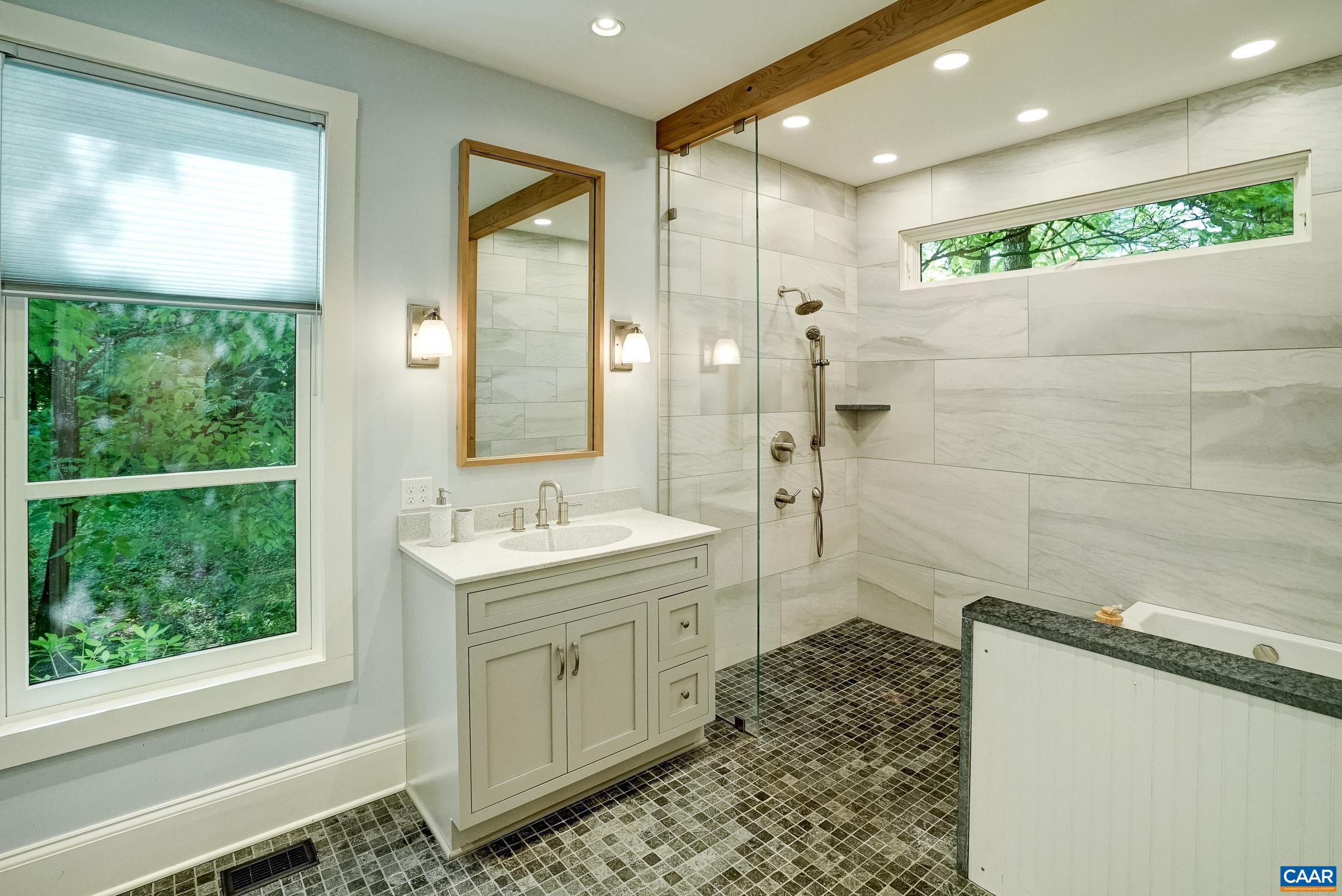 New primary bathroom with jacuzzi tub and frameless glass shower.