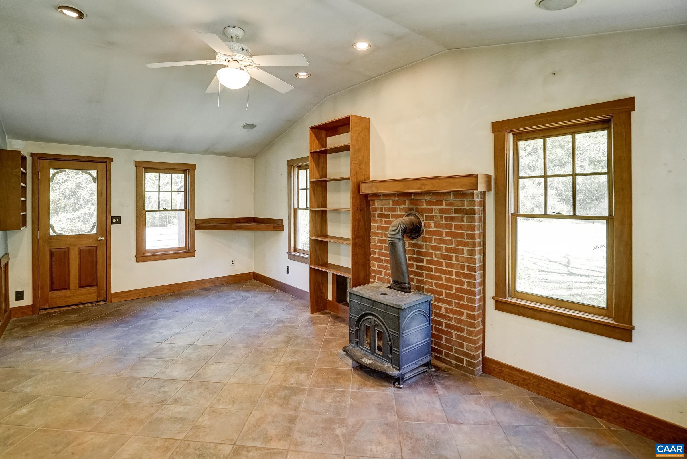 Den features ceramic tile flooring, wood stove, and built-in bookshelves.