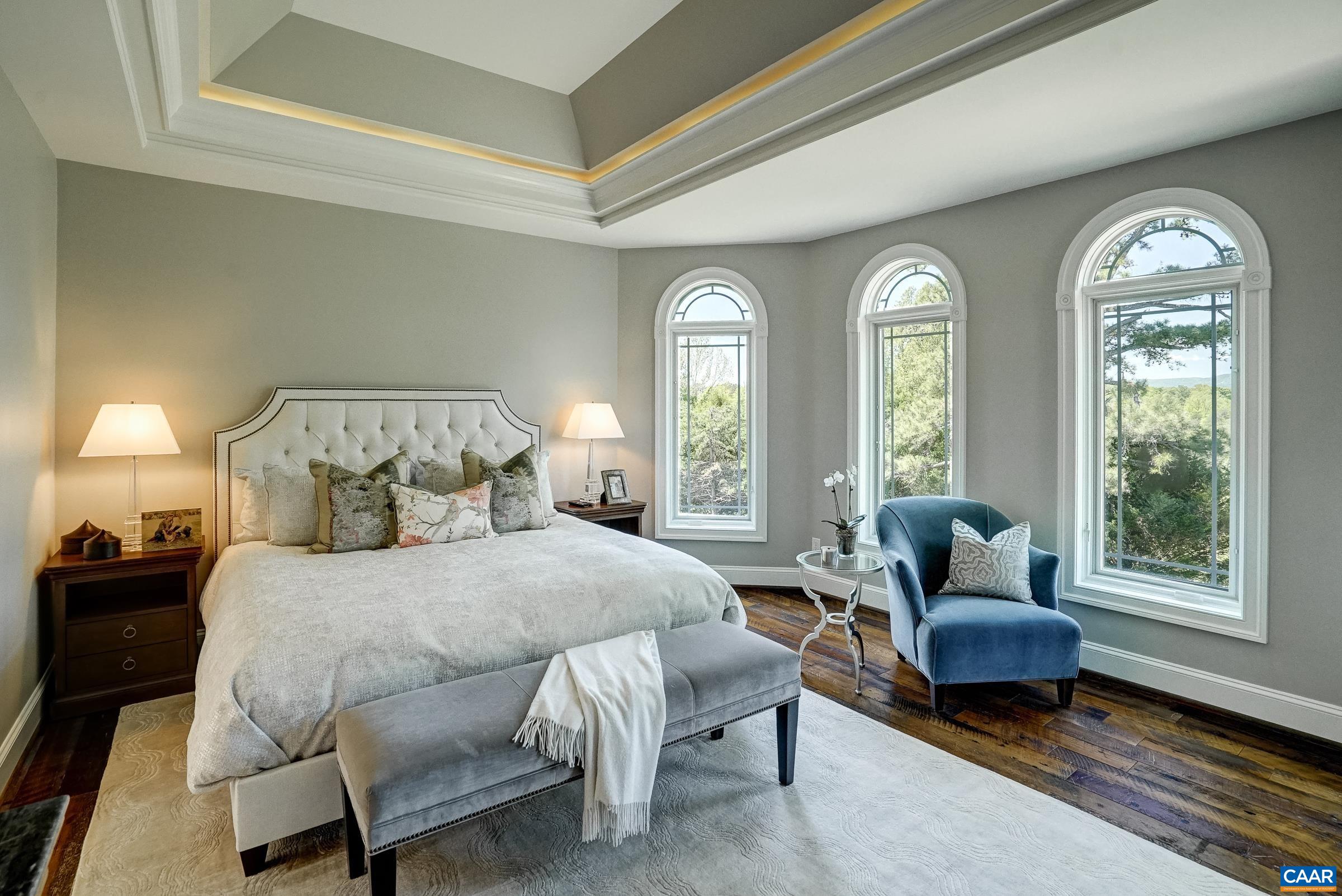 Stunning main level primary suite features a tray ceiling with calming cove lighting and arched windows to take in the view.