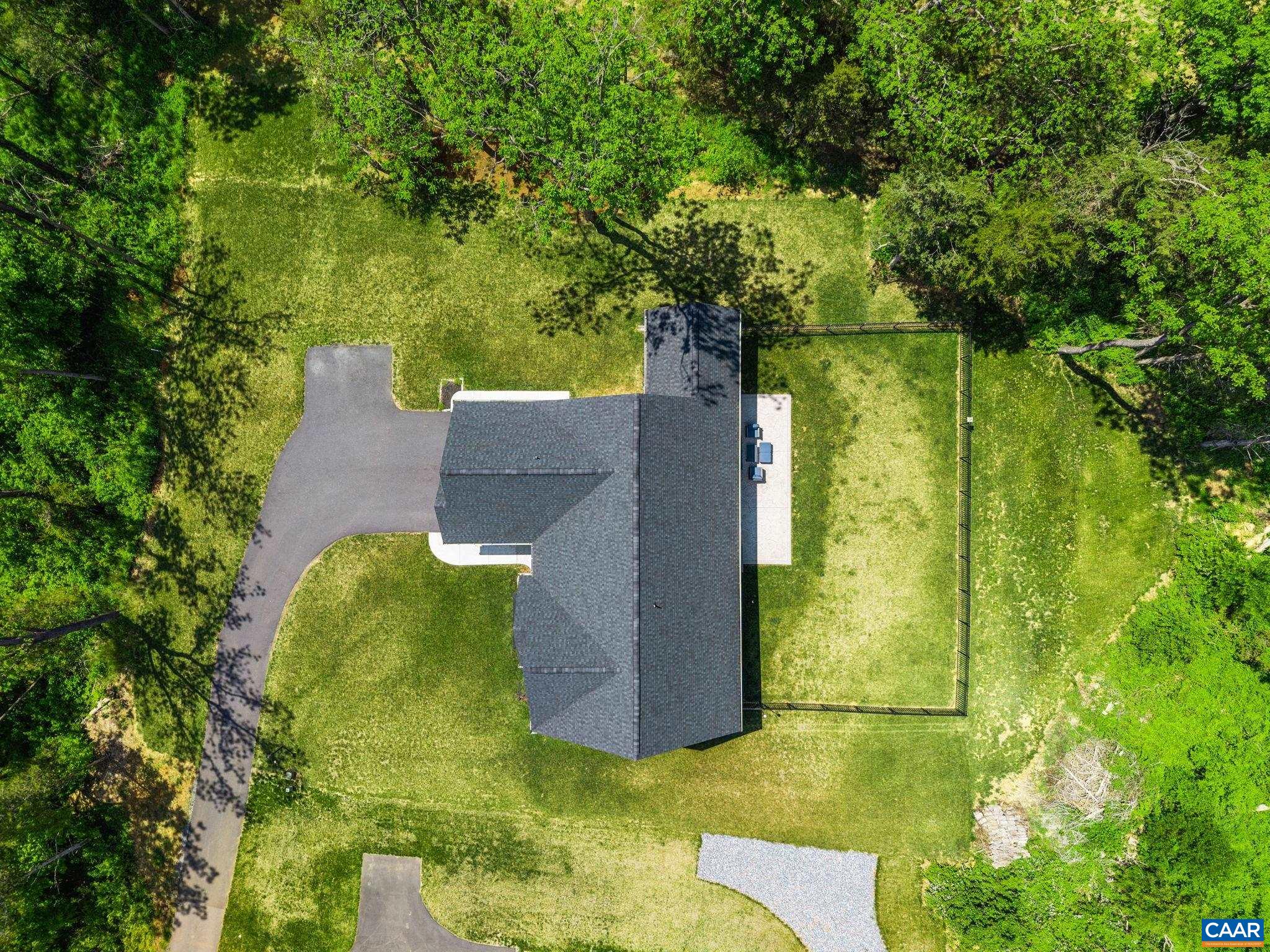 Drone view shows roof, yard, and backyard fencing.  The backyard extends beyond the fence.