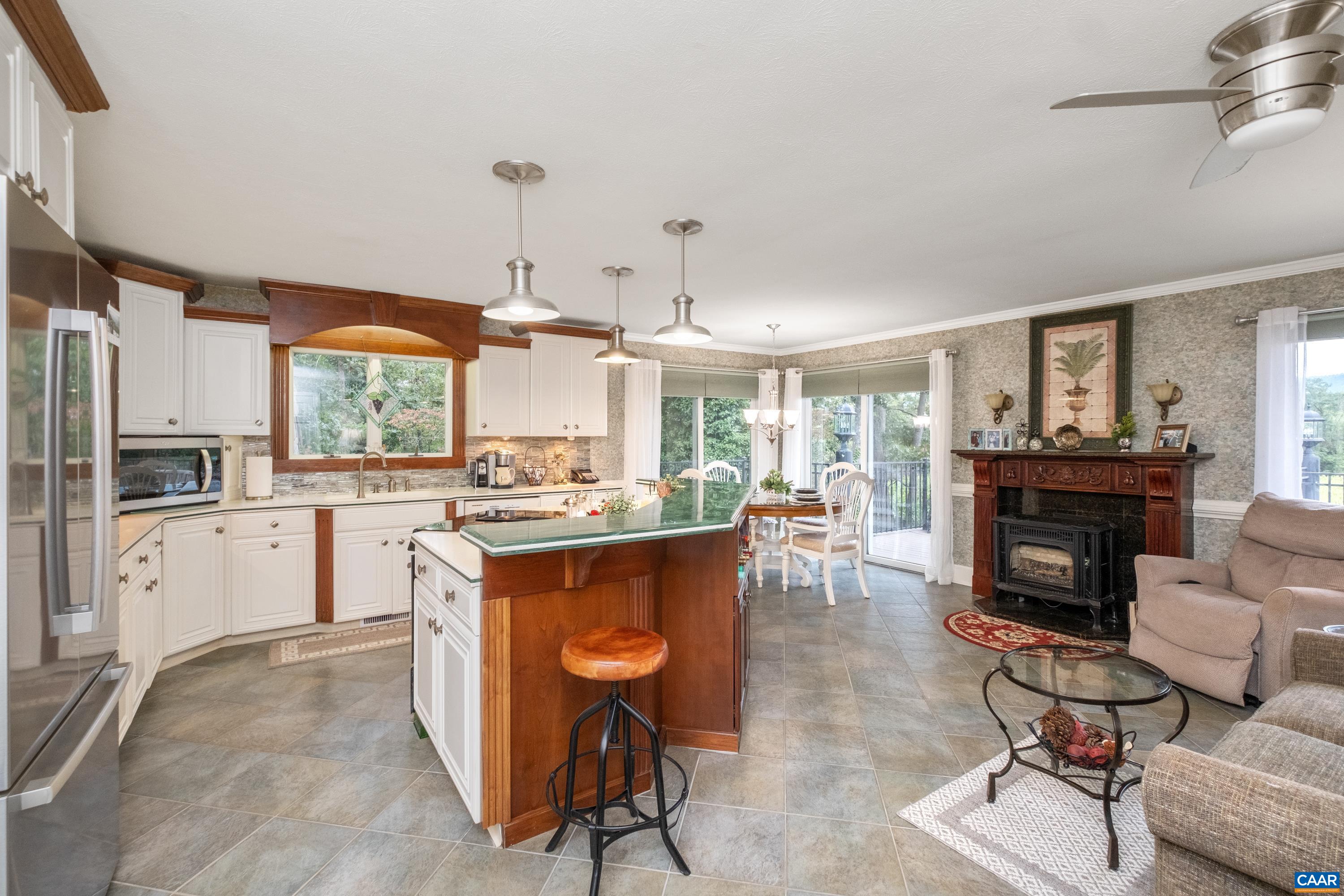 The kitchen features a sizable pantry (located behind camera), a large island with seating and a TV cabinet facing the sitting area, cherry cabinetry, white cabinetry, plenty of countertop workspace, a gas log fireplace for ambiance and warmth, and more!