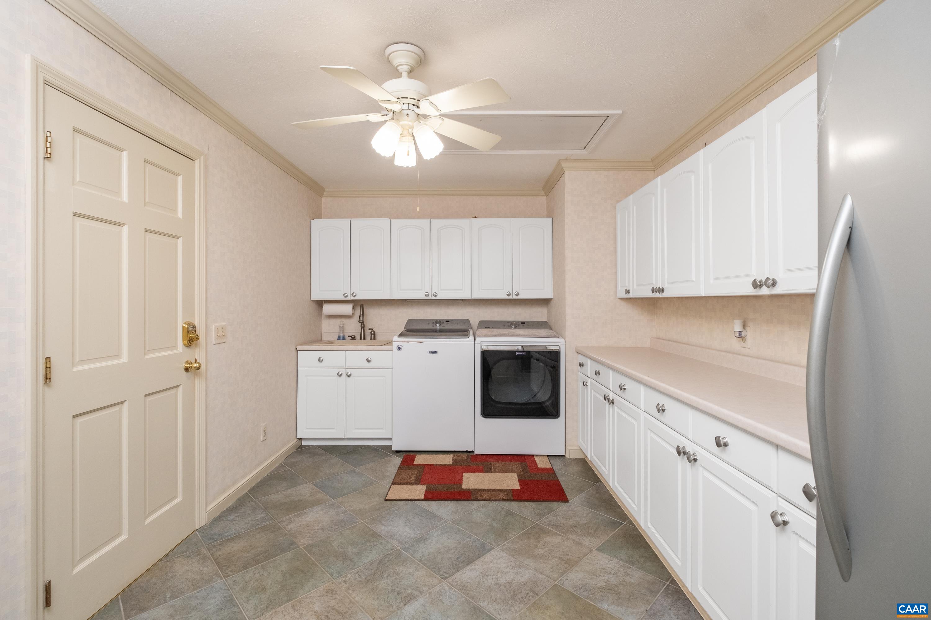 Large laundry room with cabinetry and countertop space.  In view is the doorway to the walk-in closet to primary bedroom #1.  Laundry room also includes a second refrigerator.