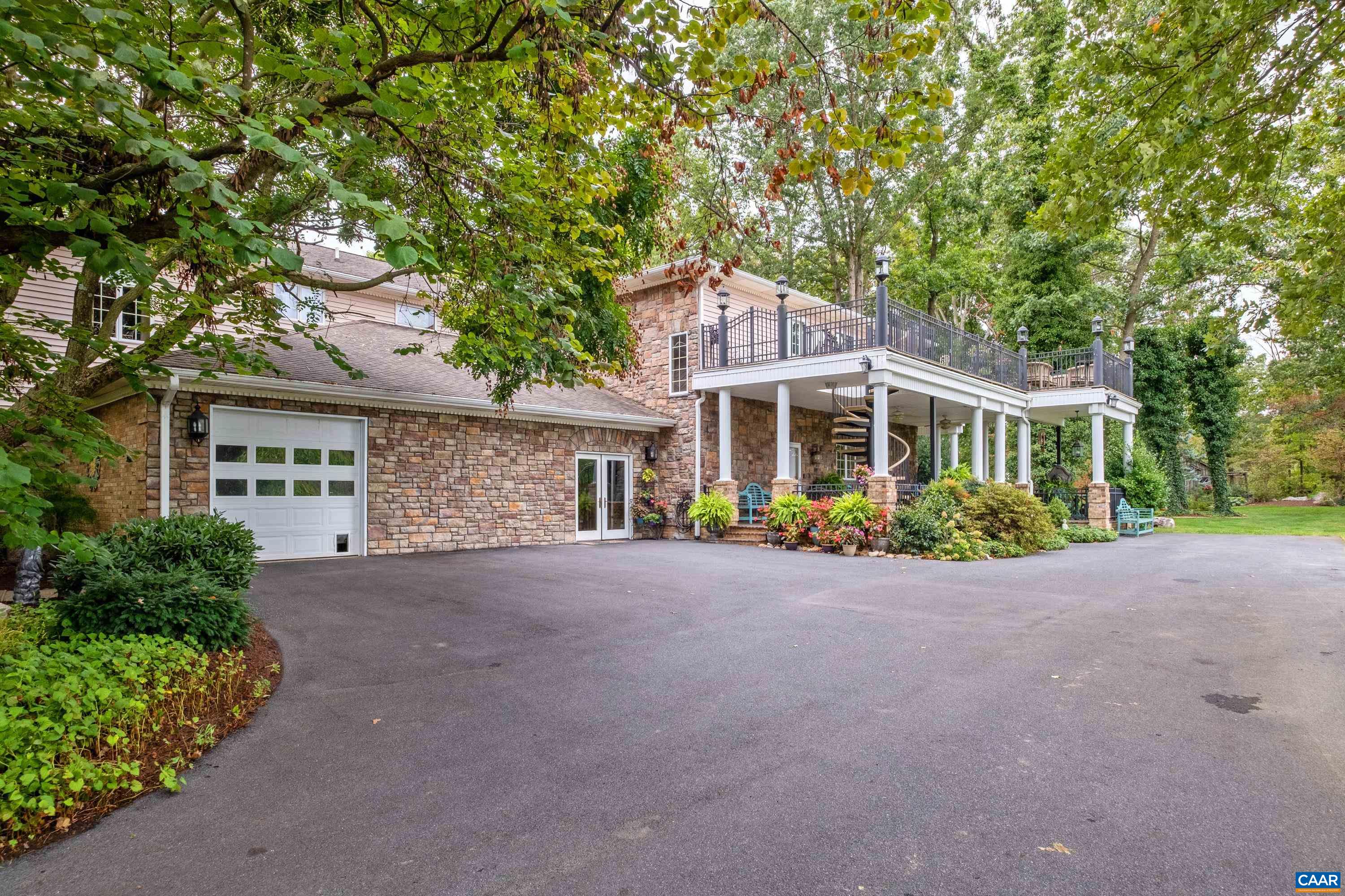 The back of the property features stone masonry, a two-bay, one garage door garage, and a covered brick patio with deck above.