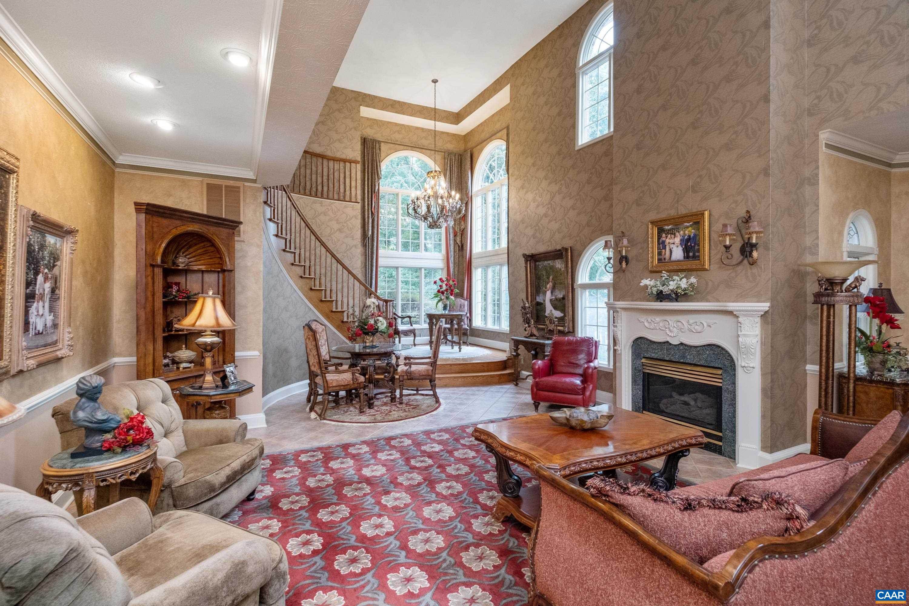 Great room features high ceilings, gas log fireplace, elegant chandelier, winding staircase, and balcony.