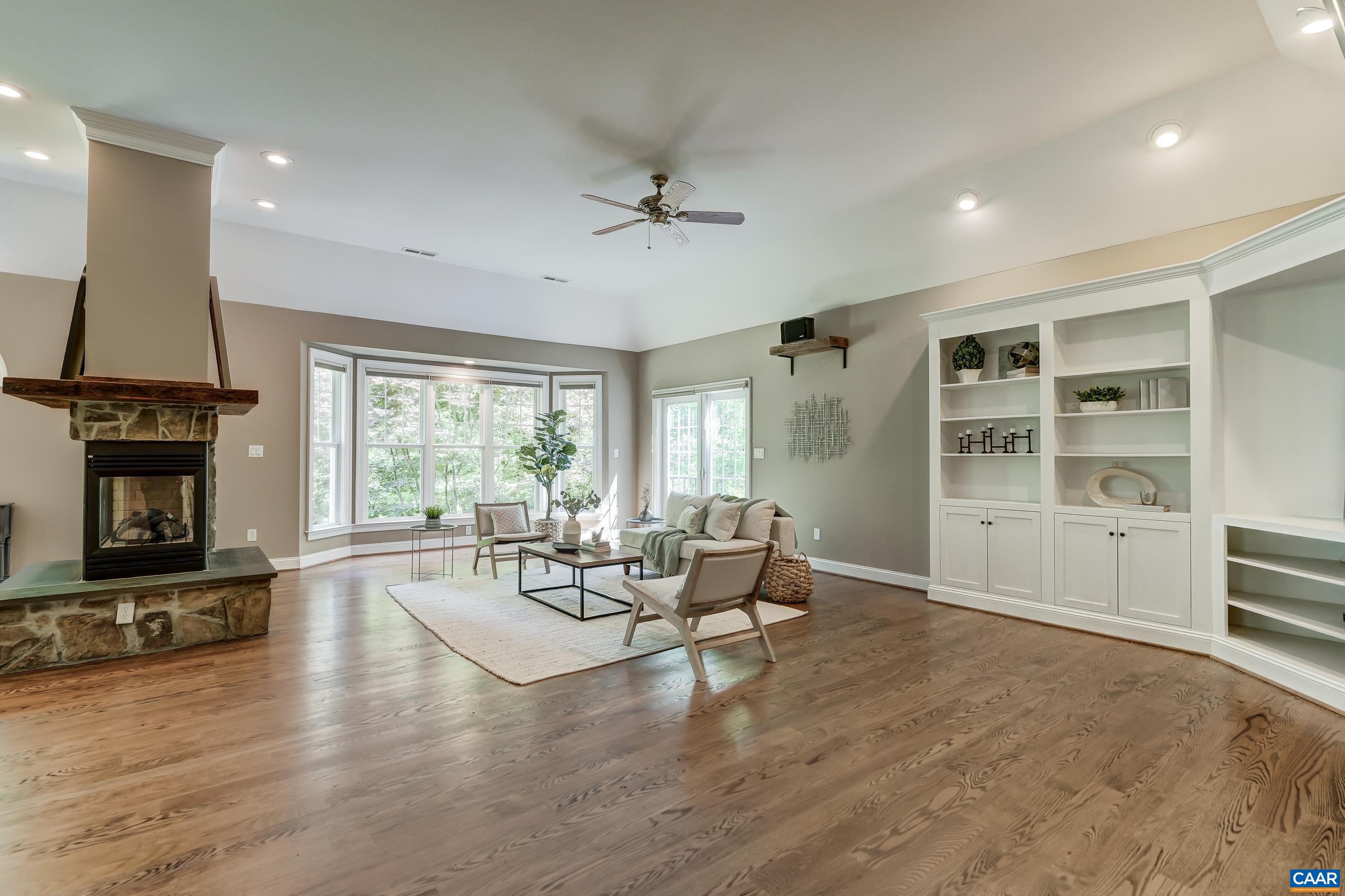 Light-filled great room features 12' ceilings with built-in bookshelves and a three sided stone fireplace.