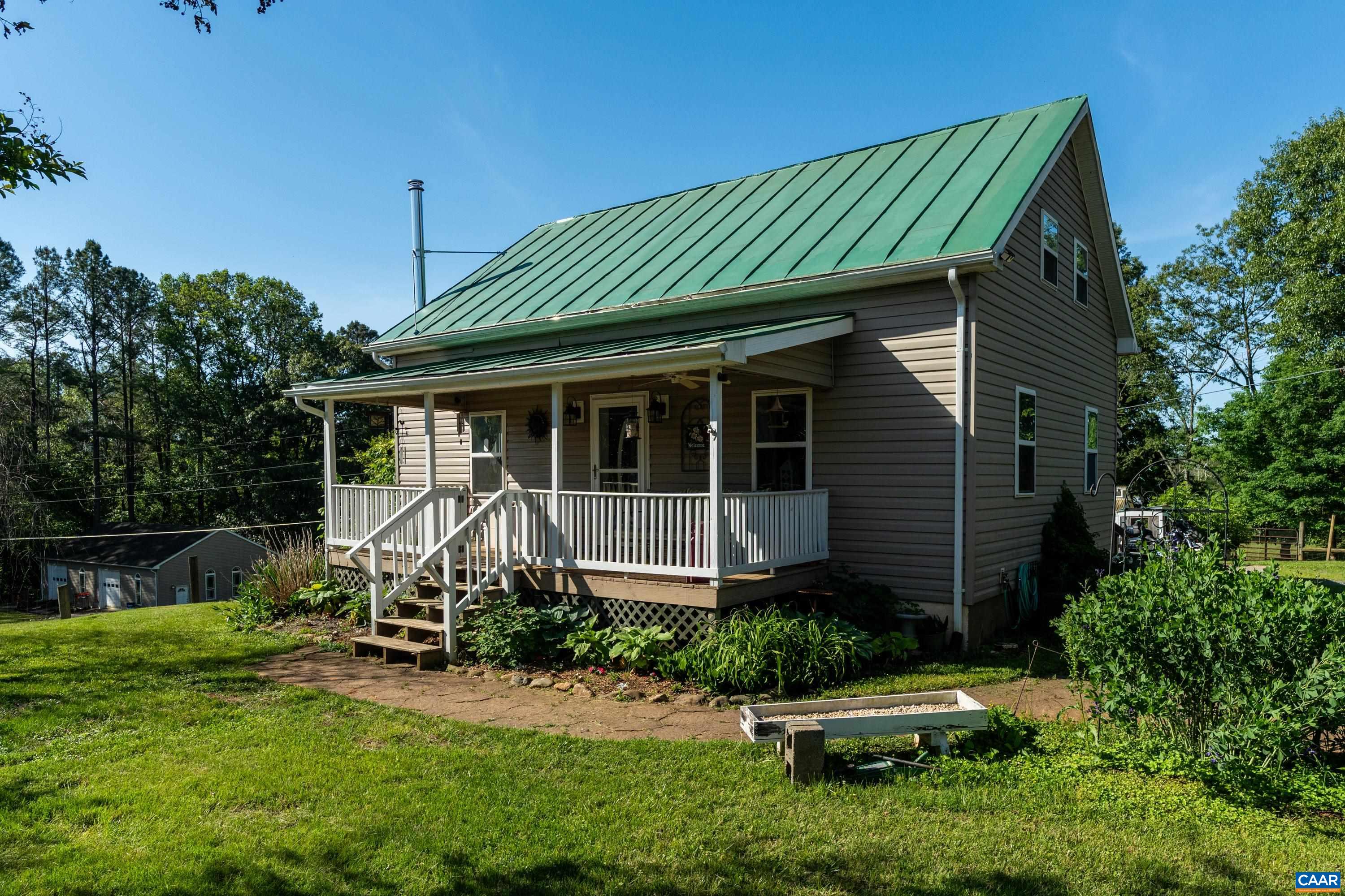 Exterior view of the home with covered front porch, metal roof, and peaceful rural backdrop. Exterior view of the home with covered front porch, metal roof, and peaceful rural backdrop.
