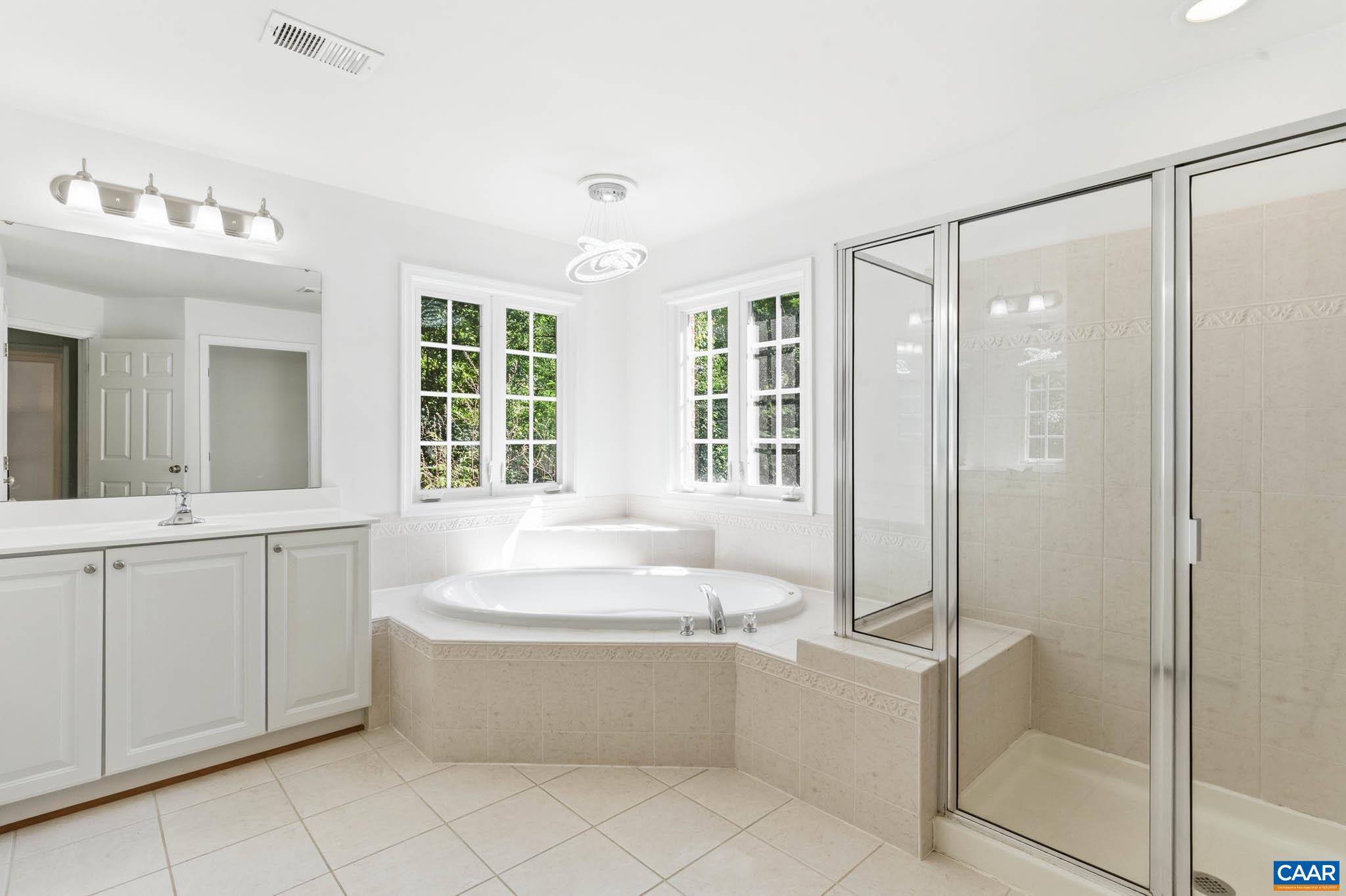 Large ensuite bath with double vanity, soaking Jacuzzi tub, separate shower, and wooded window views.