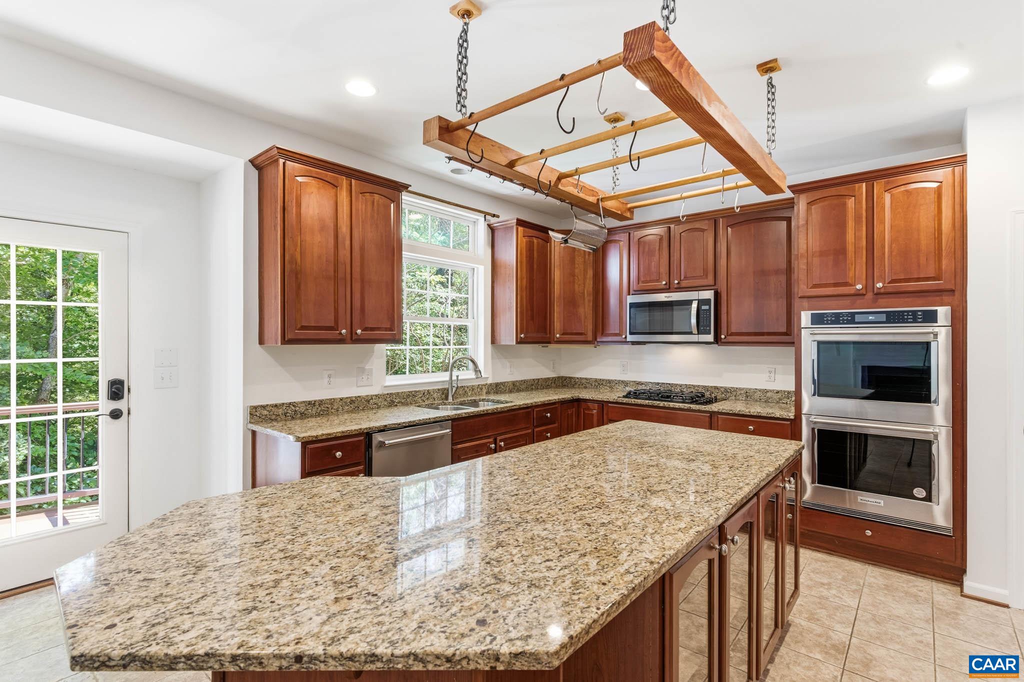 Large kitchen with central island, warm cabinetry, granite counters, stainless appliances, and access to the rear deck.