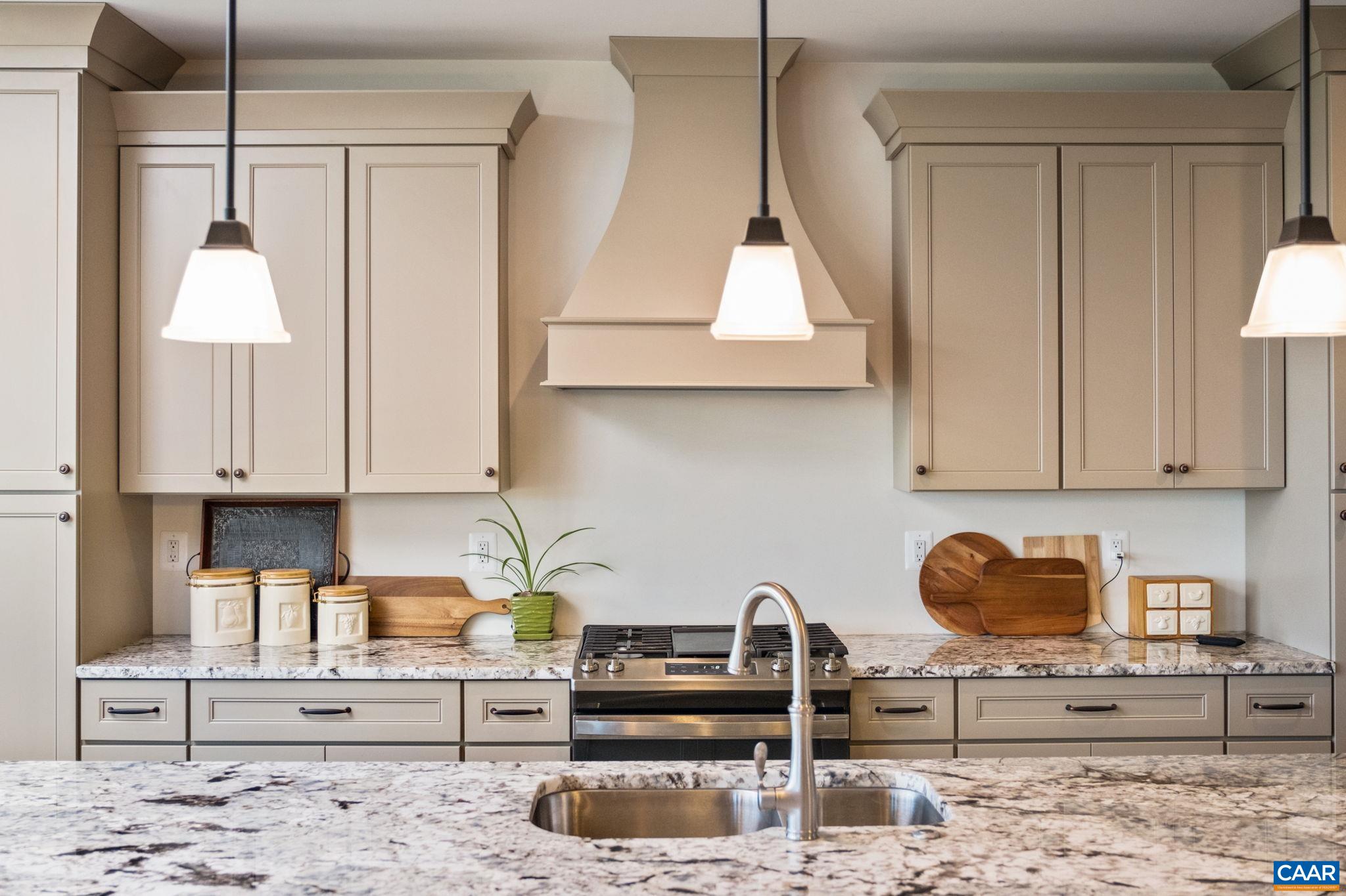 The kitchen features upgraded granite on the large island with sink and countertops, an oven hood, a gas range, and plenty of cabinetry. The walk-in pantry is just beyond the kitchen in the hallway (hallway not in view). The kitchen features upgraded granite on the large island with sink and countertops, an oven hood, a gas range, and plenty of cabinetry. The walk-in pantry is just beyond the kitchen in the hallway (hallway not in view).