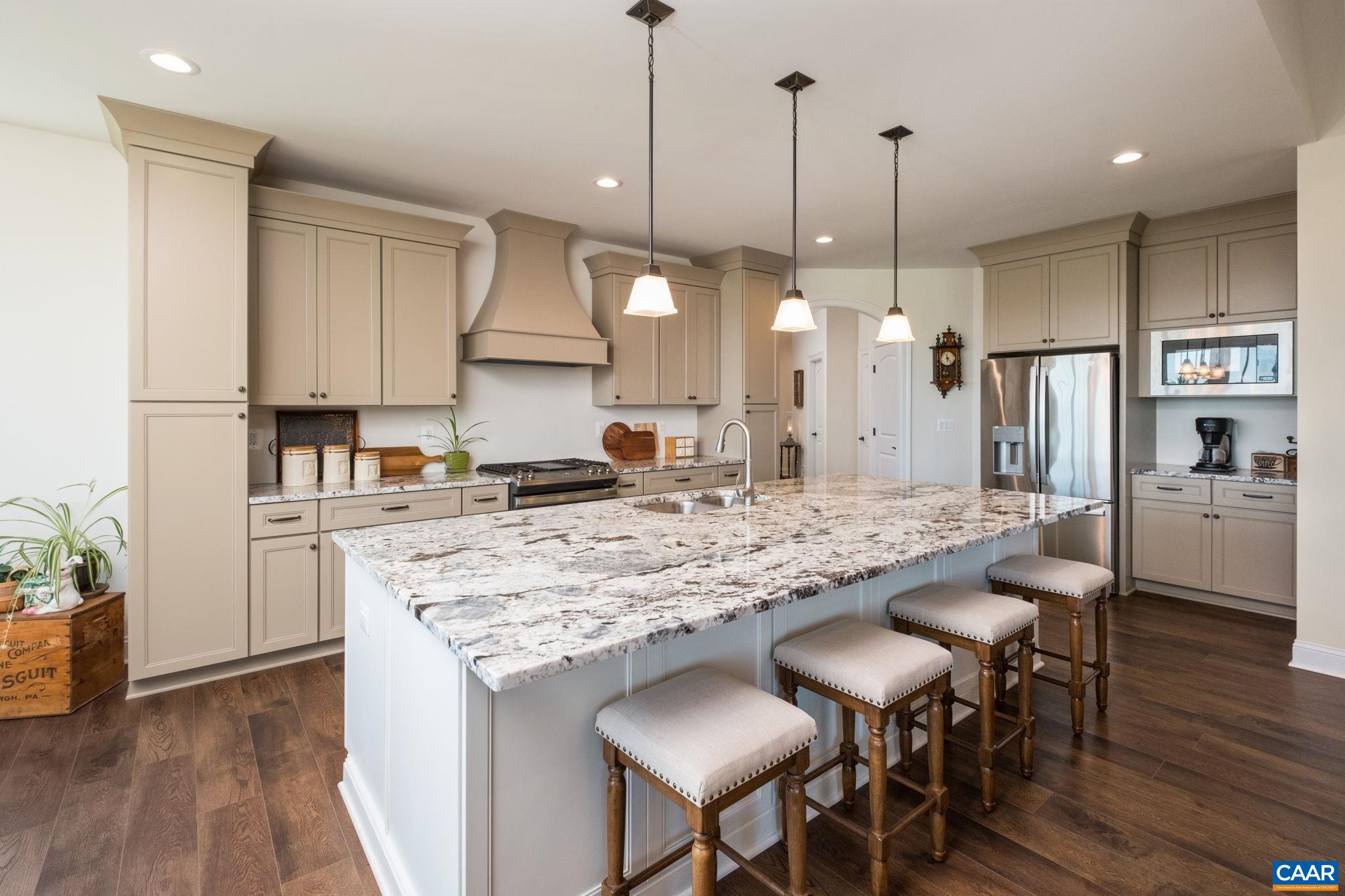 The kitchen features upgraded granite on the large island with sink and countertops, an ovenhood, a gas range, a walk-in pantry, and plenty of cabinetry. The coffee bar is in view. The kitchen features upgraded granite on the large island with sink and countertops, an ovenhood, a gas range, a walk-in pantry, and plenty of cabinetry. The coffee bar is in view.