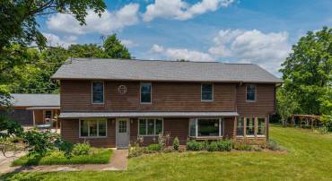 The front view highlights the spacious acreage surrounding this lovely home, large front porch, and expansive detached garage.  This home also features a large driveway for parking and landscaping.