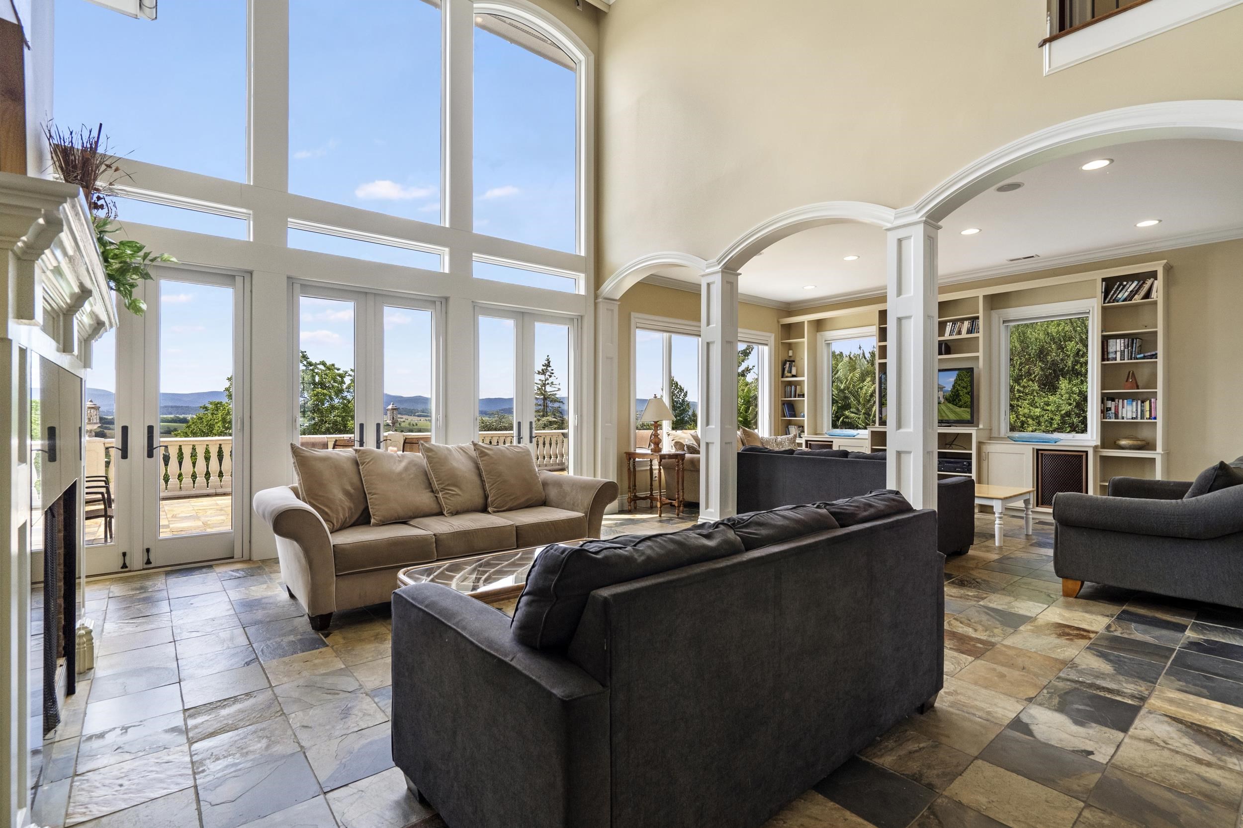 The soaring wall of windows with custom arch, have multiple doors that open this living space to the exterior expansive terrace which each have the same travertine flooring. The soaring wall of windows with custom arch, have multiple doors that open this living space to the exterior expansive terrace which each have the same travertine flooring.