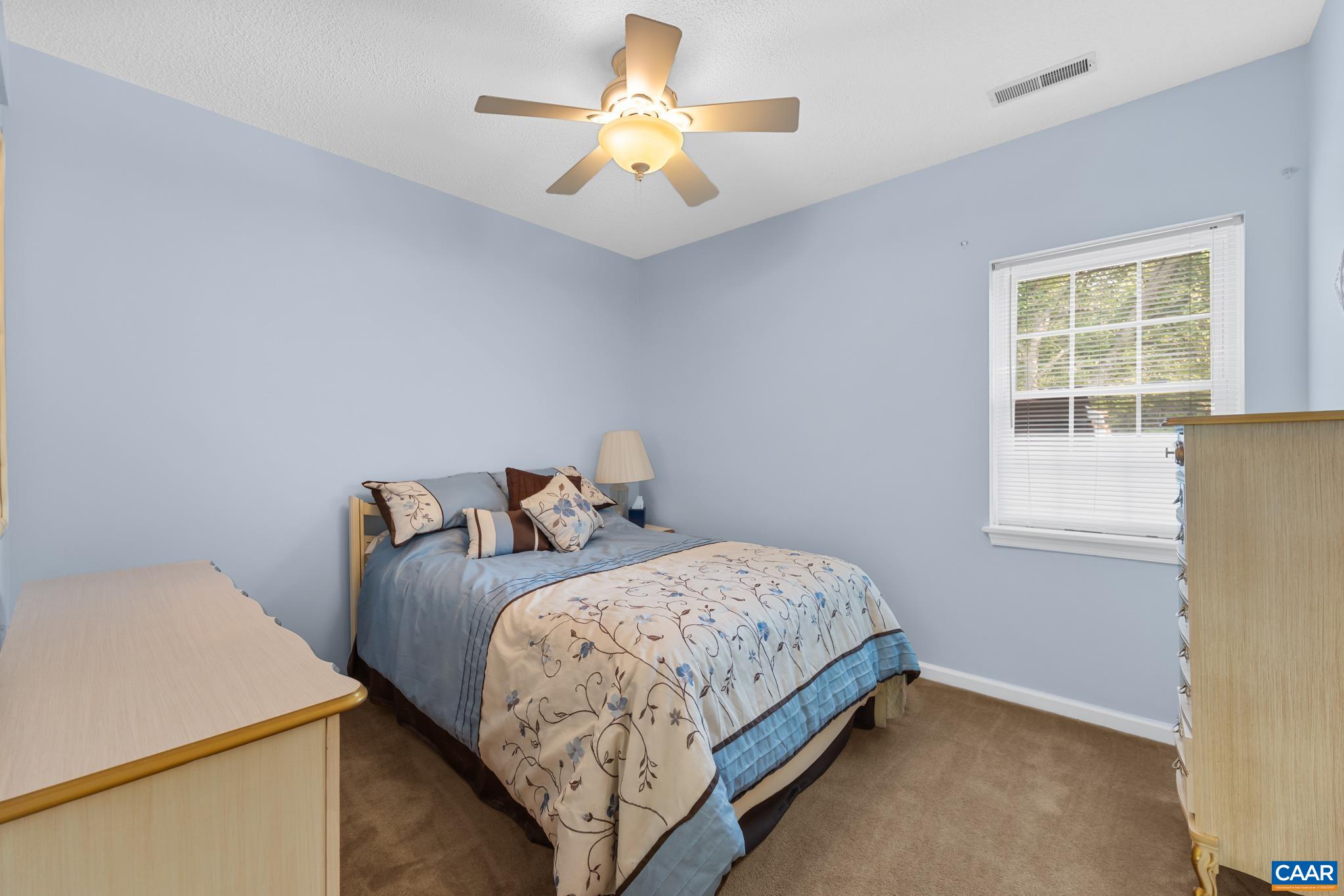 Rest easy in this peaceful bedroom retreat! Features light blue walls, soft carpeting, a classic ceiling fan, and a bright window offering pleasant outdoor views. Cozy, comfortable, and perfectly proportioned for guests or family!