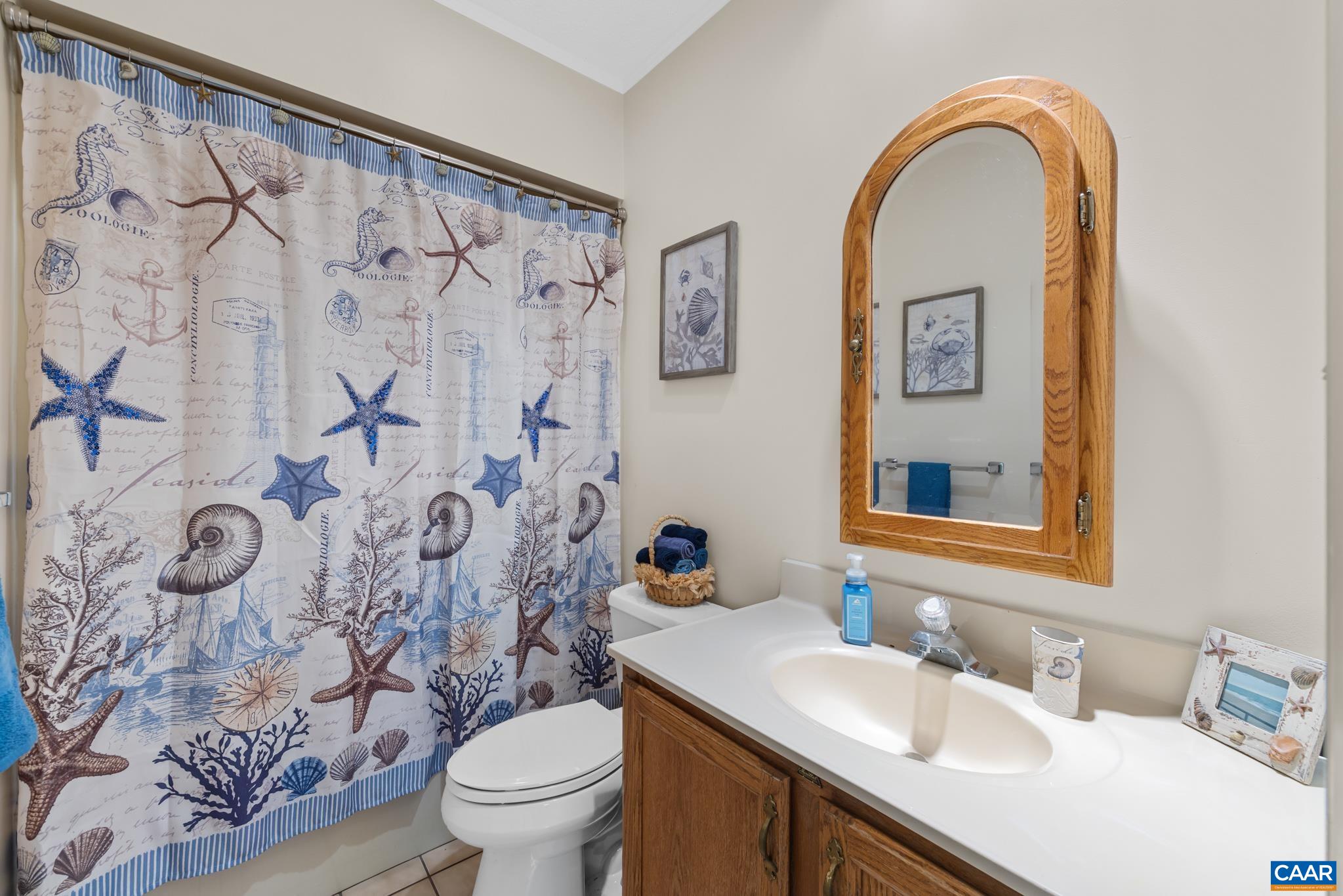 A charming and functional full bathroom! Features a oak-finished vanity, clean white countertop, arched wood medicine cabinet mirror, and tiled flooring. Perfect for family or guests!