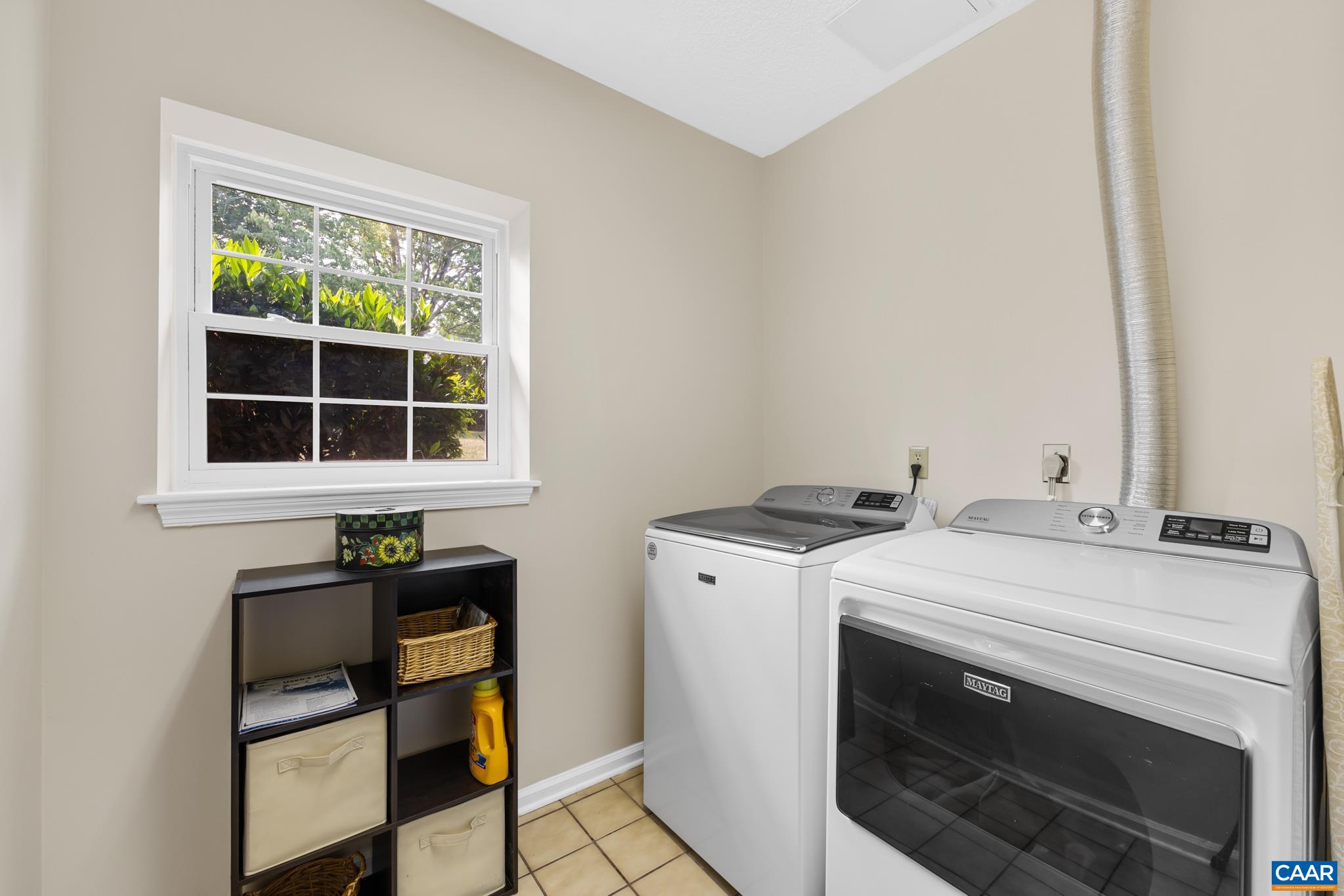 Laundry day made easy! This functional utility area features side-by-side washer and dryer units, a bright window letting in natural light, tiled flooring, and room for storage to keep your laundry routine organized and hassle-free!