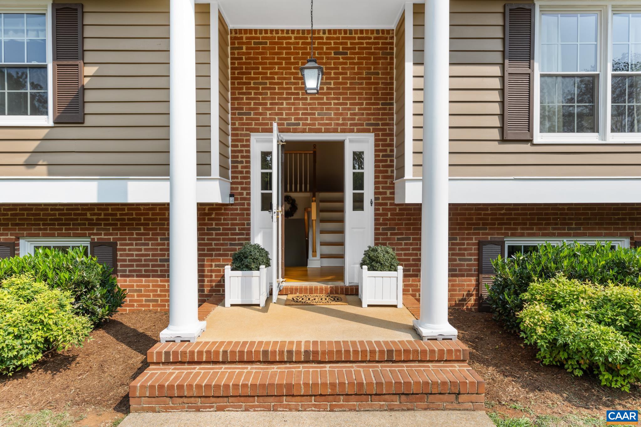 Step into elegance with this charming entryway featuring grand brick steps, classic white columns, and a welcoming front door. Warm siding, brick accents, and beautiful greenery create unforgettable curb appeal!