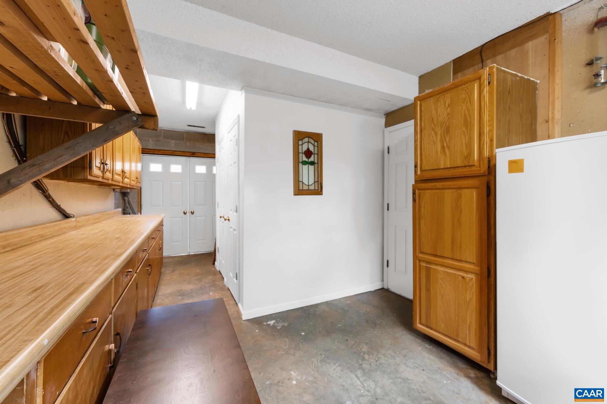 Maximize your storage and workspace! This functional lower-level utility area features an extensive wooden workbench with built-in cabinetry, overhead shelving, and extra appliance space—ideal for crafts, home projects, and organized storage!