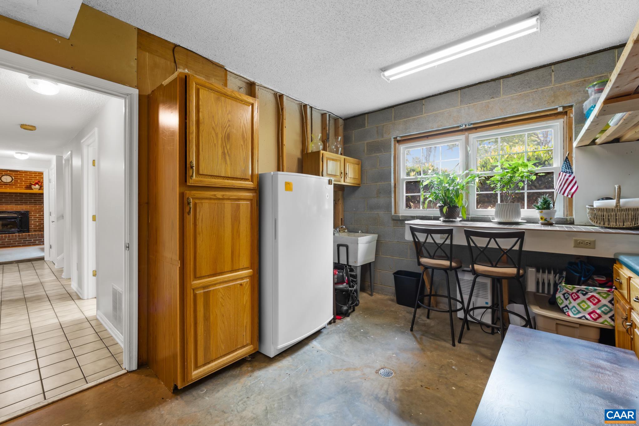 Versatile basement work and craft space! Features custom wooden cabinetry, a deep utility sink, upright freezer, built-in shelving, and a sunlit window seating bar. Perfect for hobbies, projects, extra storage, and laundry day prep!