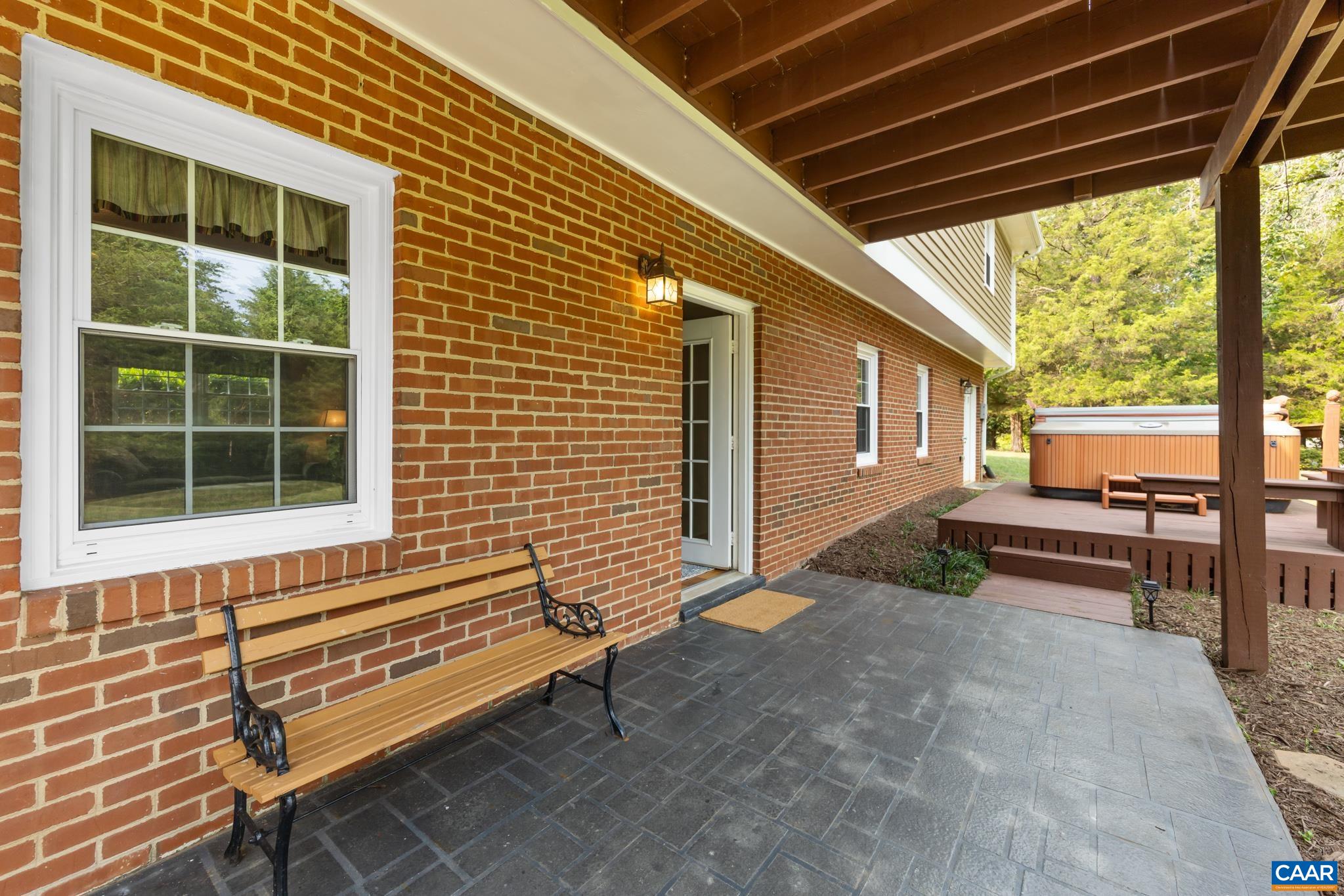 Step out into your private outdoor retreat! Features a stamped concrete patio under a covered deck, classic brick exterior, cozy seating area, and steps leading to a raised deck with a hot tub. Perfect for year-round outdoor entertaining!