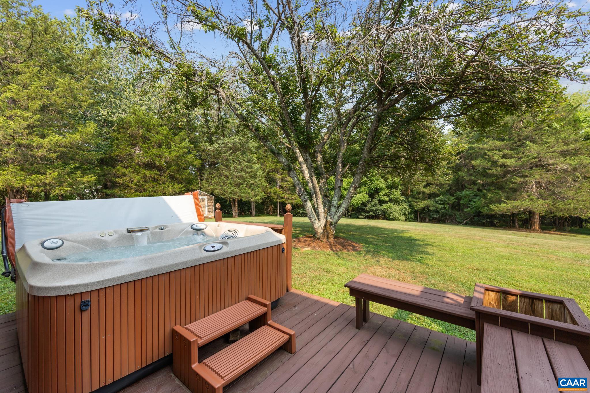 Unwind in luxury! This private deck features a multi-jet hot tub with convenient access steps, integrated wooden bench seating, and built-in planters. Set against a lush, grassy yard with mature trees—your personal backyard sanctuary!