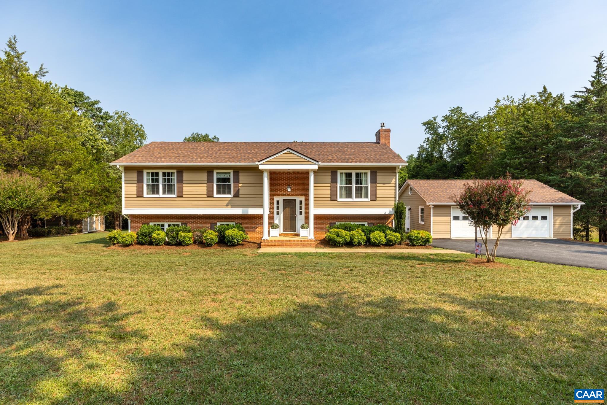 Picture-perfect curb appeal! Welcome to this beautiful home featuring a lush front lawn, manicured landscaping, covered front portico, wide paved driveway, and an attached garage—all set against a serene, tree-lined backdrop!