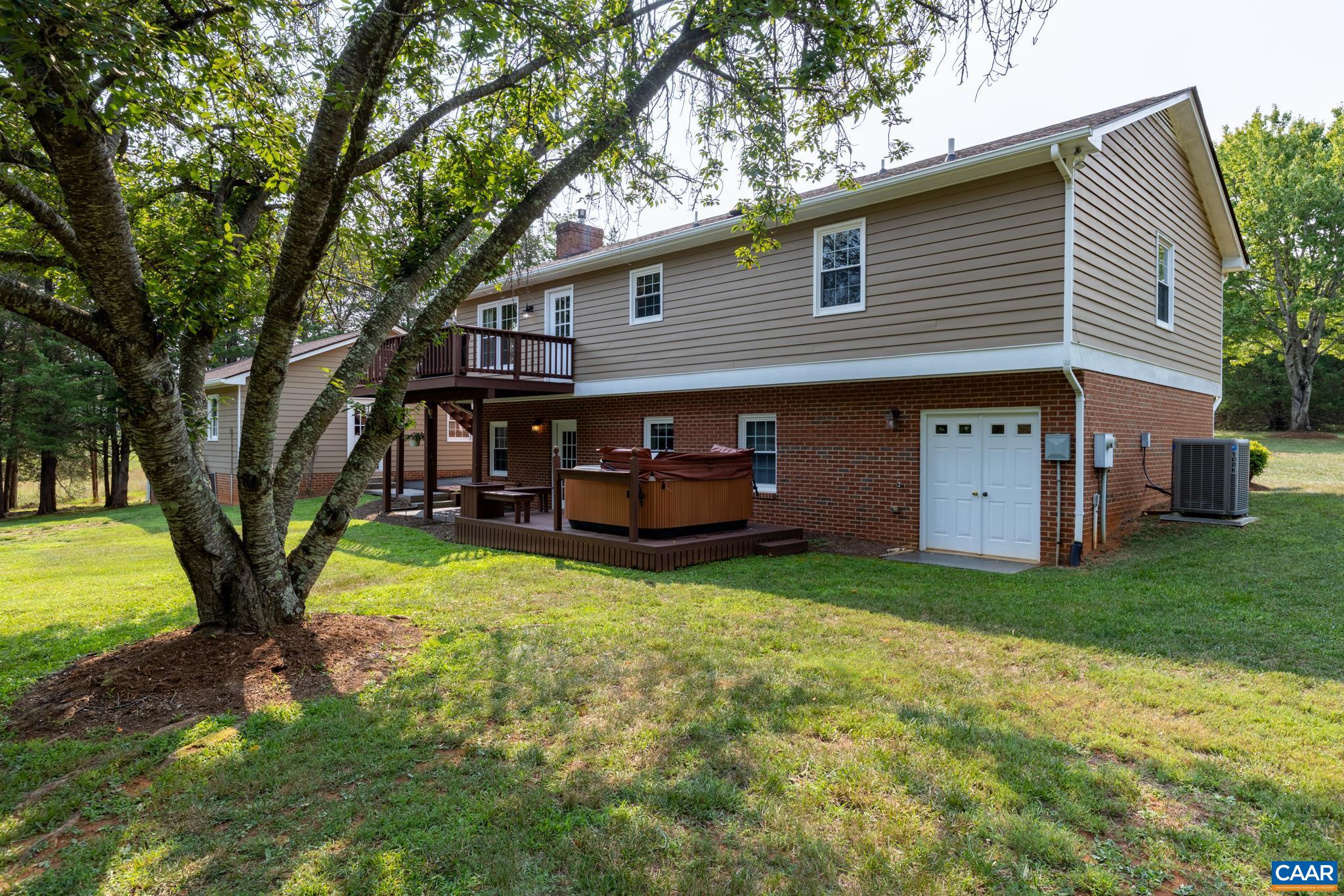Your private backyard oasis awaits! Unwind on the spacious elevated deck, relax in the private hot tub, and enjoy a sprawling, tree-lined lawn. Features durable siding, brick accents, and convenient lower-level garage access for ultimate living!