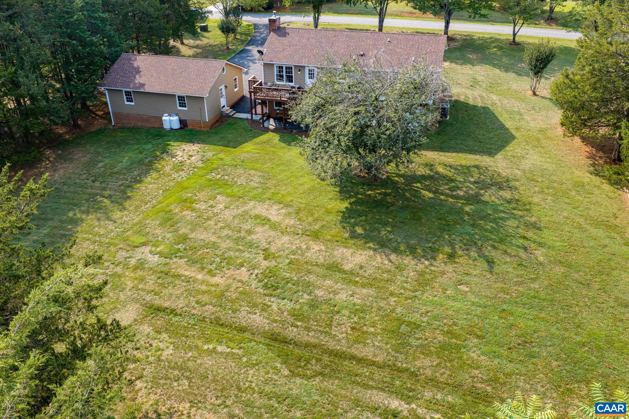An expansive private sanctuary! High-angle view highlighting a vast, sun-drenched yard, mature trees providing natural shade, and a multi-level back deck overlooking the grounds. Endless room for outdoor recreation, gardening, and relaxing!
