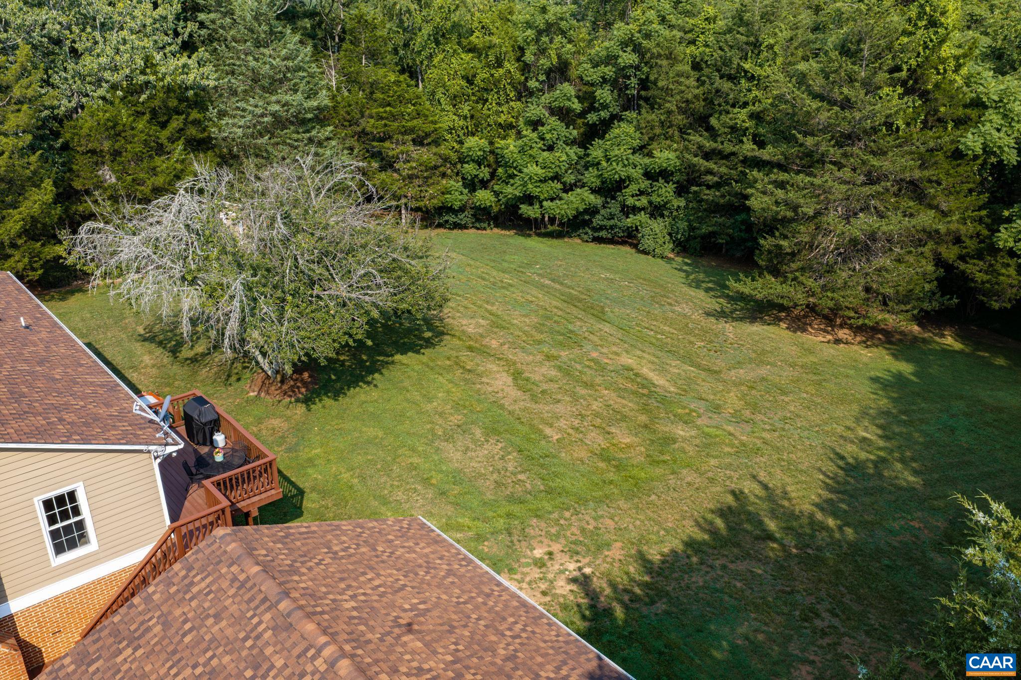 Expansive aerial view showcasing a massive, sun-drenched lawn bordered by dense green woods! Features a view of the back roofline and wooden deck. Perfect for outdoor recreation, private gardening, or simply enjoying nature!