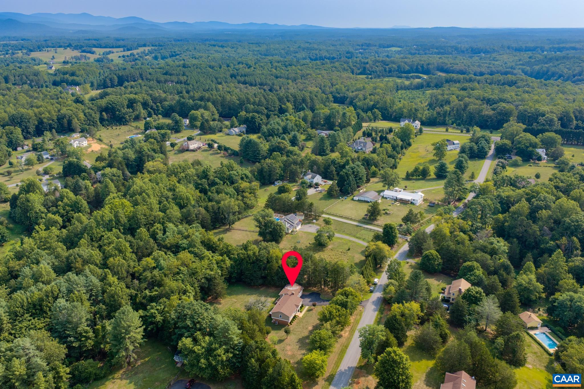 Spectacular wide aerial view showcasing the home nestled in a scenic, rolling landscape! Surrounded by lush green tree lines, open countryside, and blue mountain horizons in the distance. An extraordinary, private setting with endless beauty!