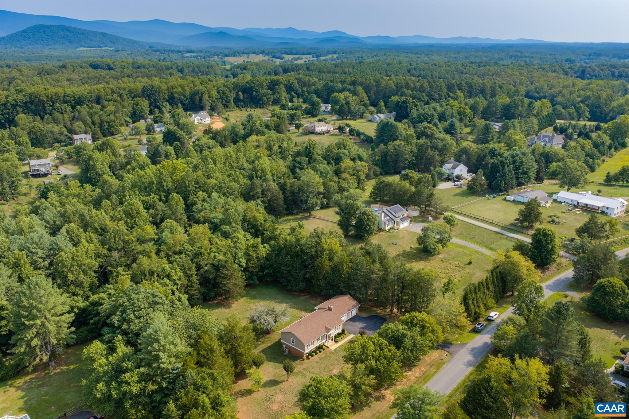 Breathtaking panoramic aerial view! Showcases the home nestled in a serene countryside setting with lush green tree canopies, rolling hills, and majestic blue mountains on the horizon. Peaceful, private living surrounded by natural beauty!