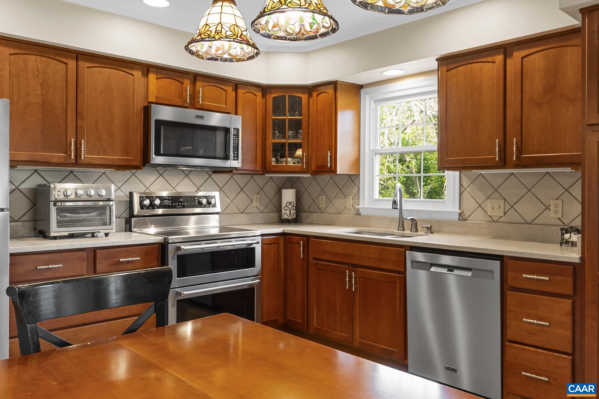 Cook and entertain with ease in this spacious kitchen! Featuring cherry wood cabinetry, stainless steel appliances, granite counter & stylish tile backsplash. Charming stained-glass lights and bright natural sunlight make this inviting space truly shine!