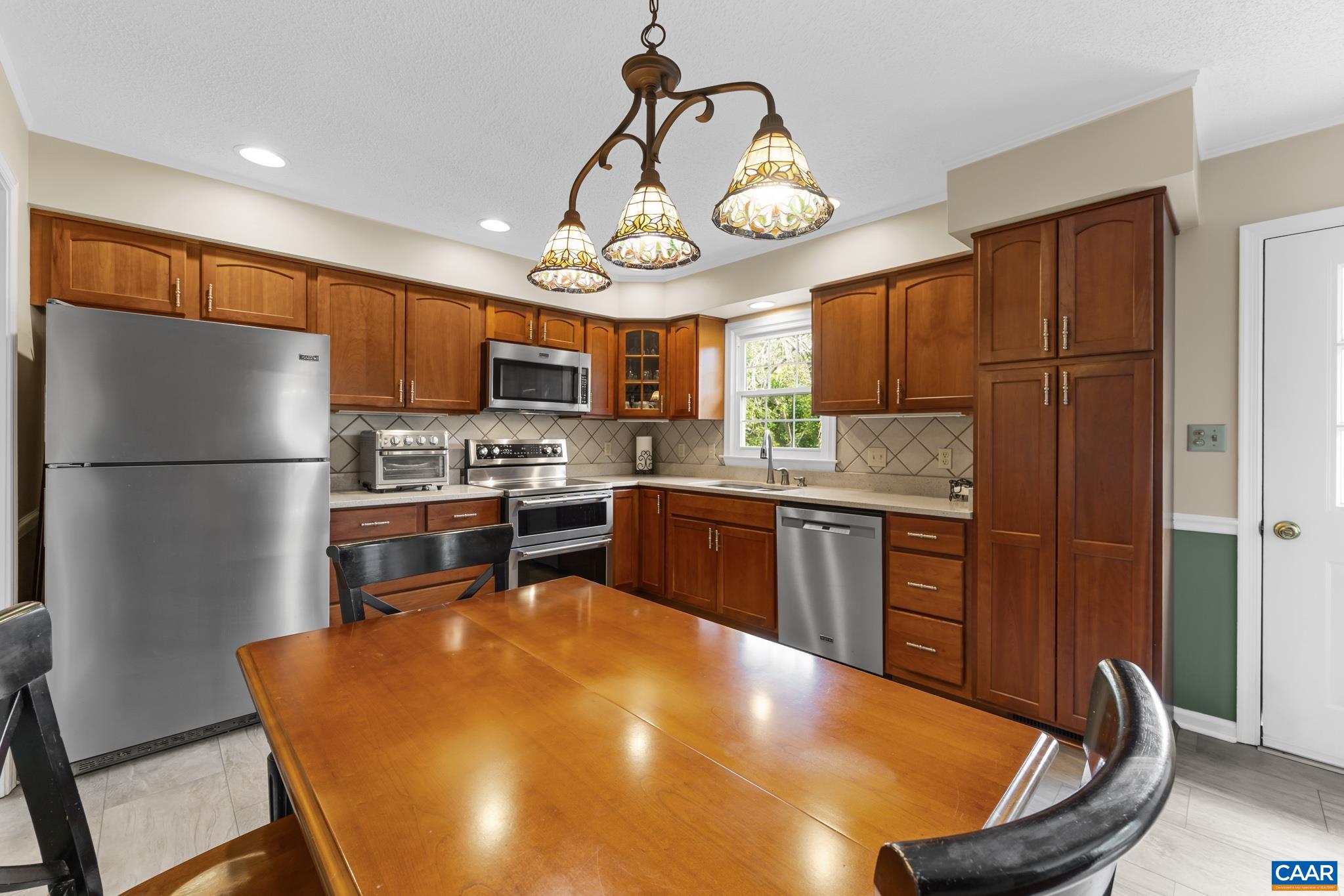 Gather around in this inviting dining area right off the kitchen! Highlighting a large wooden dining table under charming stained-glass pendant lighting, rich cherry cabinetry, and stainless steel appliances—perfect for everyday meals and entertaining!