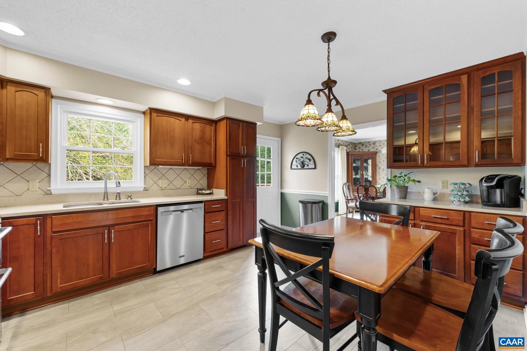 This light-filled eat-in kitchen combines style and functionality! Features handsome wood cabinetry, stainless steel appliances, modern flooring, and a cozy dining area with elegant hanging light fixtures. Perfect for quiet meals or casual gatherings!