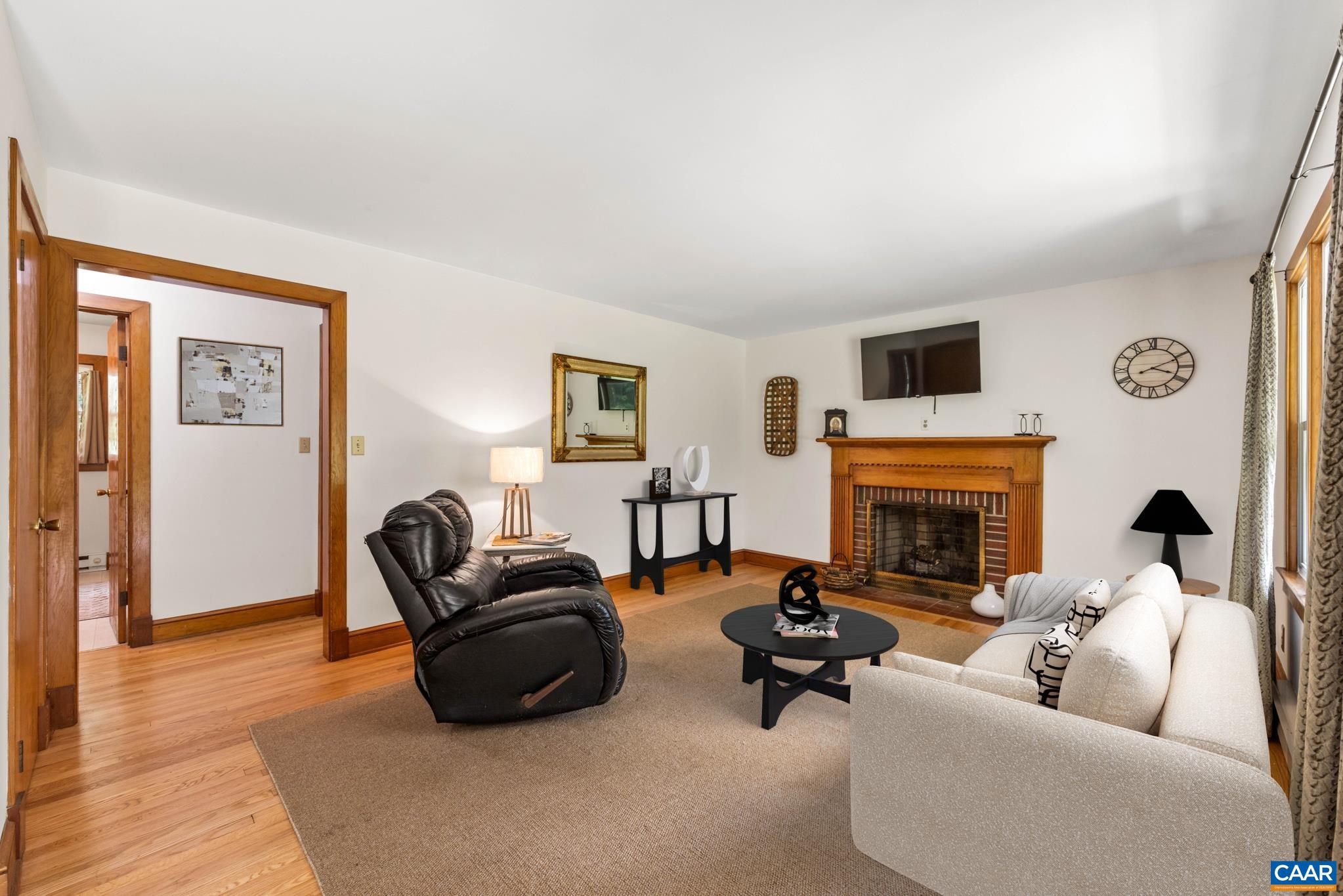 Welcoming living room with gleaming hardwood floors, a wood-burning fireplace, and a large bay window framing scenic countryside views. This room has been virtually staged to showcase the potential and help you imagine yourself at home.