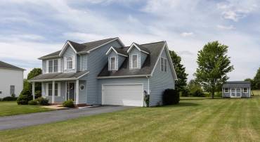 The front view of this home located in the Three Leagues subdivision highlights the two-car garage, front porch, large asphalt driveway, and landscaping.