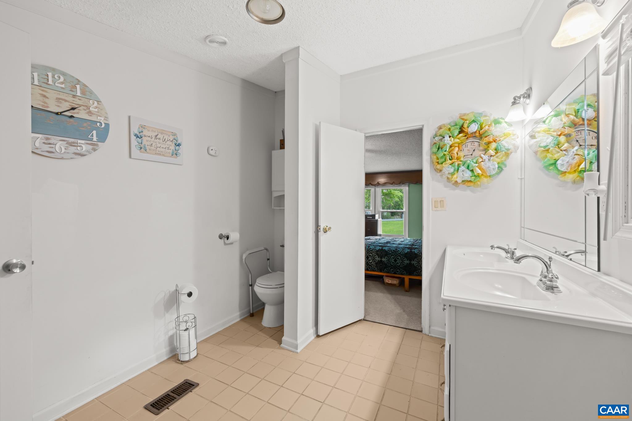 Bright, functional full bathroom featuring a large double-sink vanity, expansive mirror, and neutral tiled flooring. A practical layout offers quick access to the adjoining the primary bedroom, making daily morning routines a breeze!