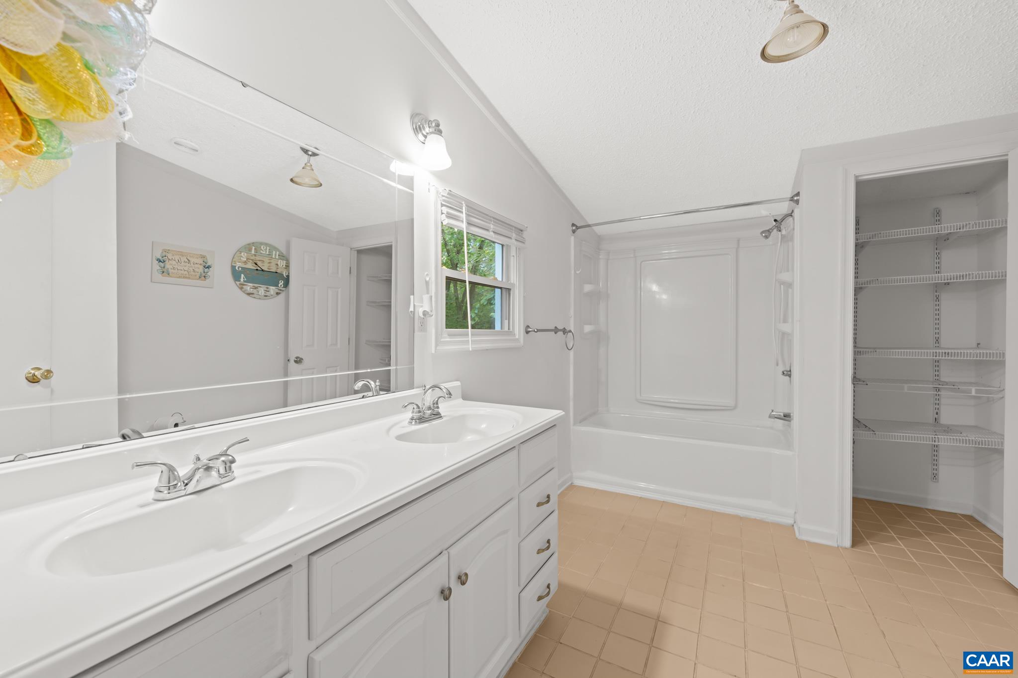 Well-appointed main bathroom featuring a long double vanity with bright vanity lighting, a tub/shower combo, and a built-in wire shelving alcove for convenient linen storage and everyday organization. Clean, functional, and move-in ready!