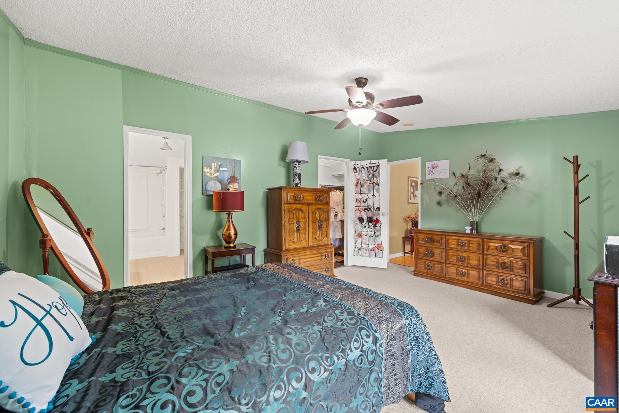 Restful Primary Suite with serene sage green walls, plush carpeting, and a cool ceiling fan. Enjoy a spacious, light-filled layout with generous furniture space, a private ensuite bath connection, and peaceful comfort for ultimate relaxation!