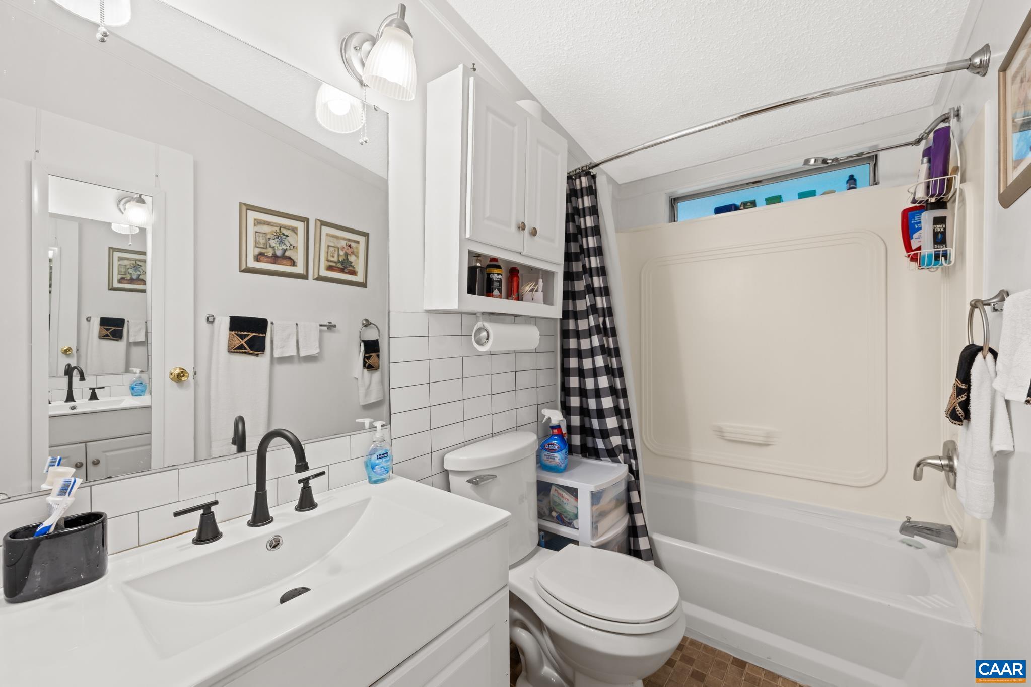 Crisp and inviting full hall bath featuring a stylish white vanity with modern black fixtures, classic subway tile accent, a tub/shower combo, and natural lighting above the shower. Includes wall-mounted storage cabinet—ideal for family and guests alike!