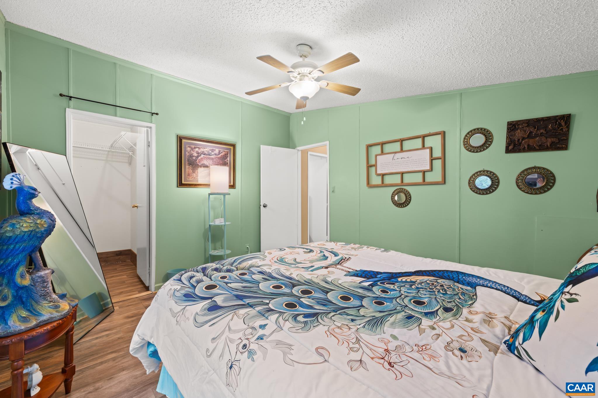 Vibrant and stylish bedroom featuring soothing sage green walls, rich wood-look flooring, and a breezy ceiling fan. Complete with a full walk-in closet and generous natural light, this cozy sanctuary is the perfect place to rest and unwind!