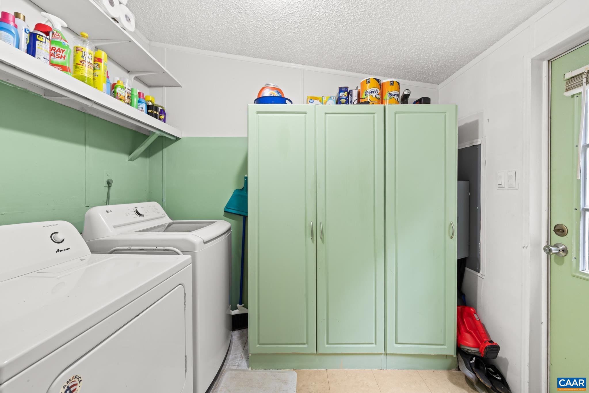 Functional laundry room and mudroom space featuring side-by-side appliances, overhead shelving, and stylish sage green storage cabinets! Includes a convenient exterior entry door for easy access and organized, stress-free daily routines.
