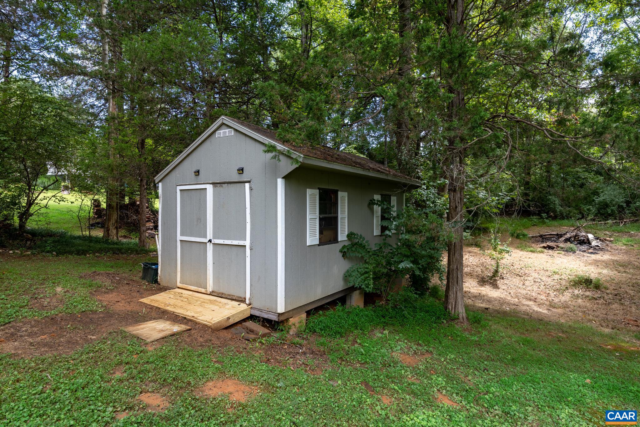Versatile outdoor storage shed with ramp entry and charming window shutters! Nestled in a peaceful, tree-lined setting, it provides ample space for lawn equipment, tools, bikes, or a workshop setup—adding great practical value to the home!