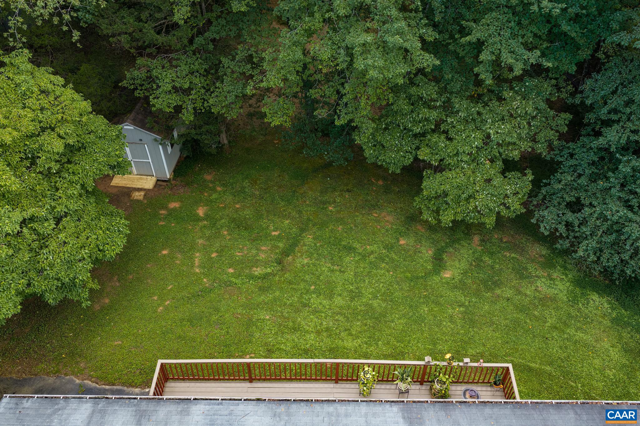 Aerial bird’s-eye view of a private, sprawling backyard! Featuring a raised rear deck overlooking a lush green lawn, mature shade trees, and a detached storage shed. An incredible secluded lot offering ultimate privacy and outdoor potential!