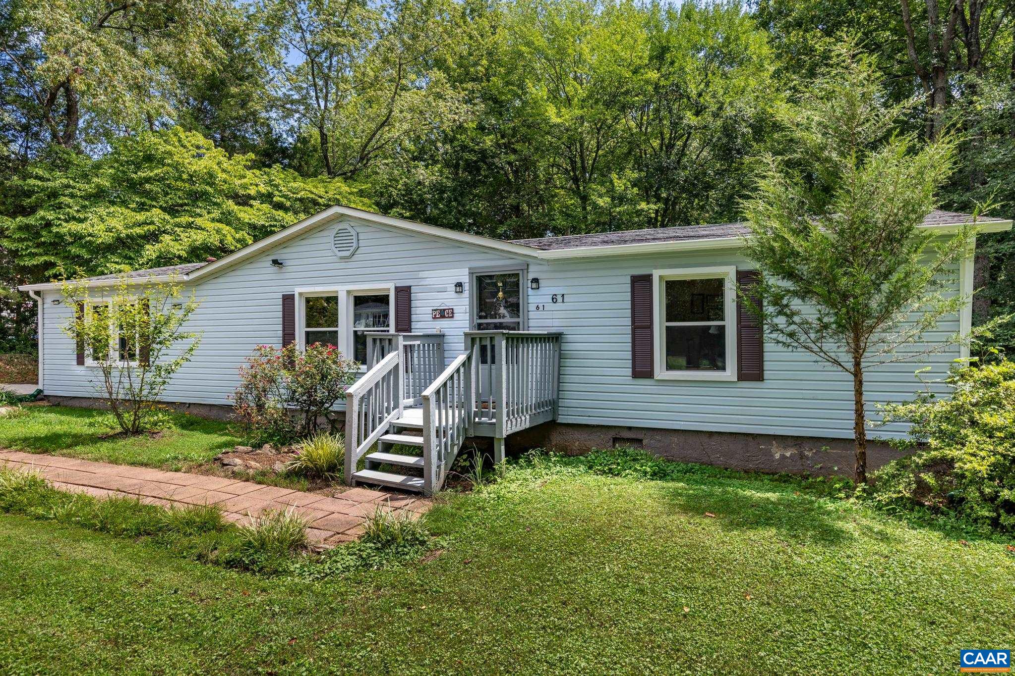 Inviting single-story home featuring light siding, contrasting dark shutters, and a cozy wooden front porch. Nestled on a lush green lawn with mature shade trees, it offers classic suburban charm, peace, and timeless curb appeal!