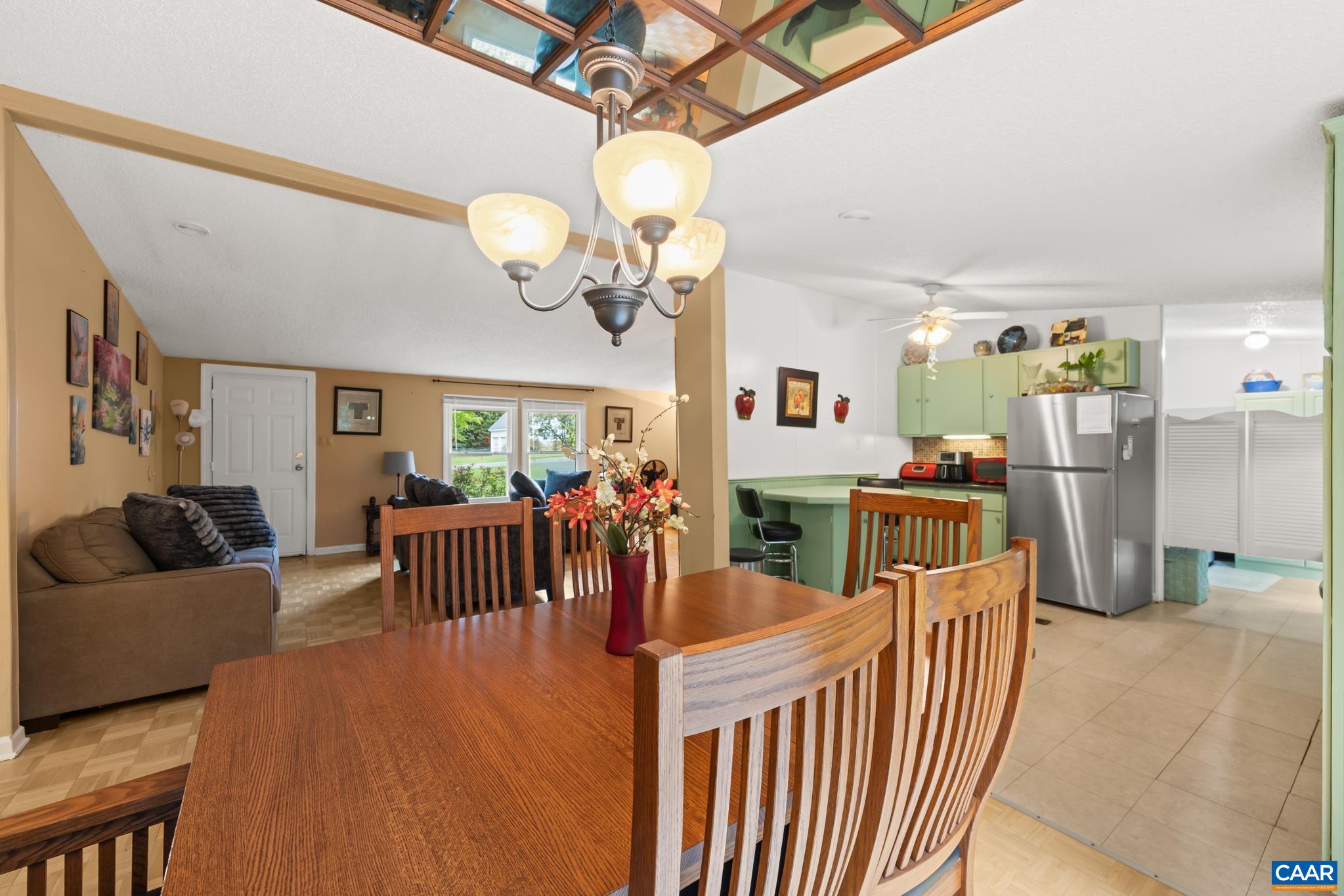 Enjoy seamless entertaining in this warm, open-concept dining space. Featuring natural wood tones, classic chandelier lighting, and exposed ceiling beams, it flows effortlessly into a bright kitchen—ideal for gathering friends and family!