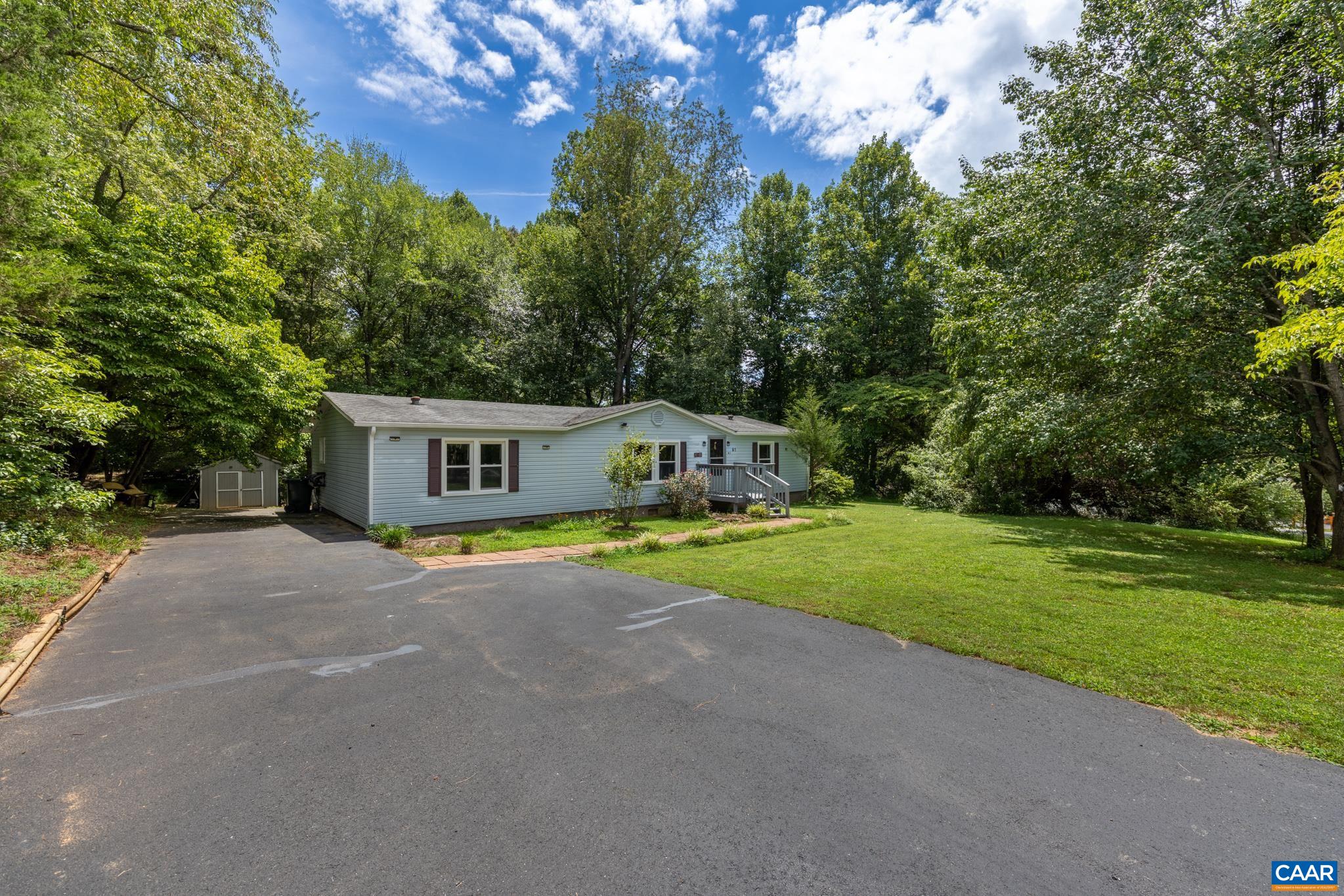 Private, peaceful setting! Featuring an expansive paved driveway with ample parking, a lush green lawn, and a mature tree-lined backdrop, this charming single-story home combines convenient parking with quiet, nature-filled suburban living.