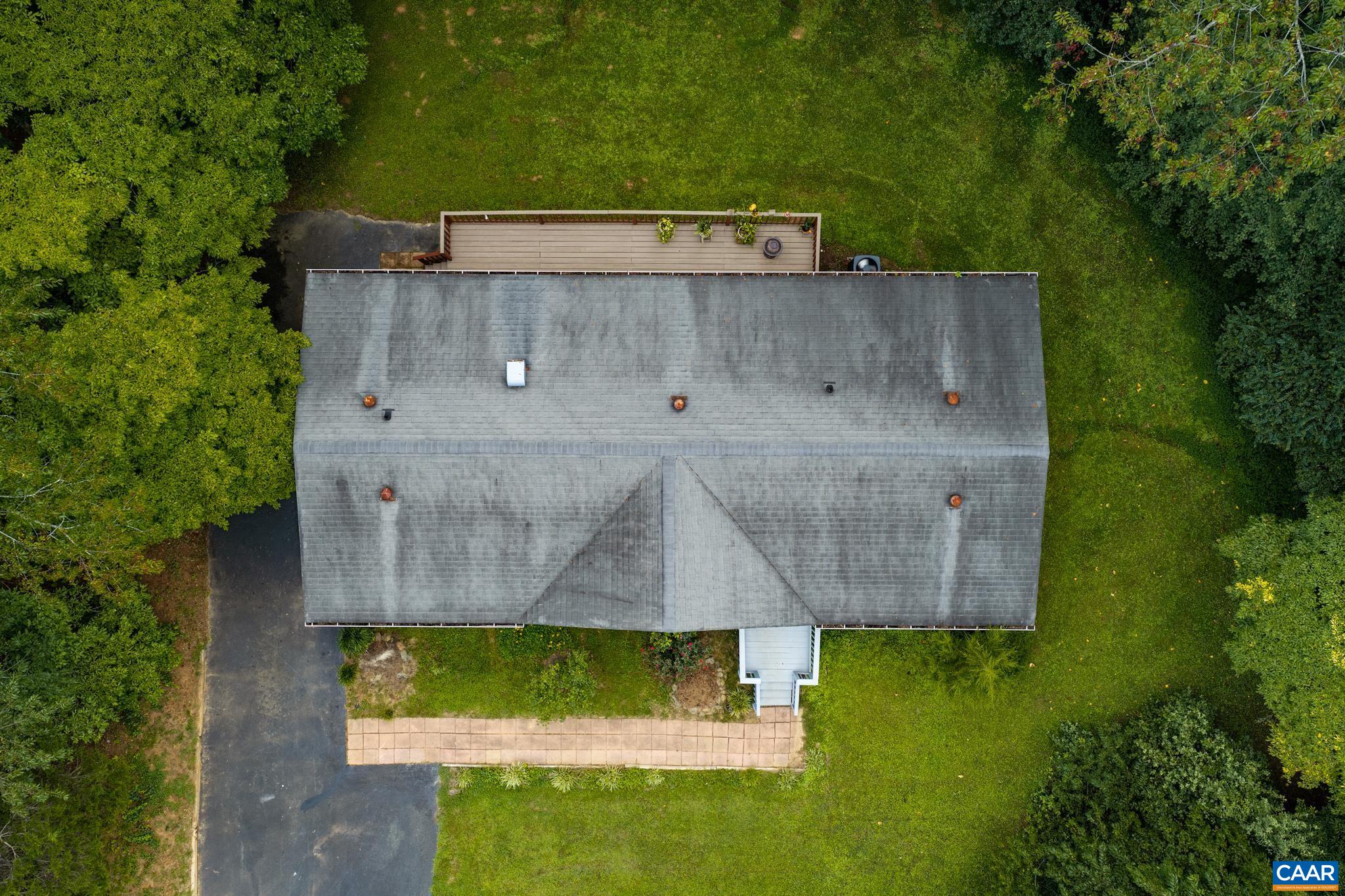 Stunning aerial view showcasing the home's private, wooded setting! Highlights include an expansive rear deck, paved walkway, and lush green lawn framed by mature trees—giving a full perspective of this quiet, scenic suburban retreat!