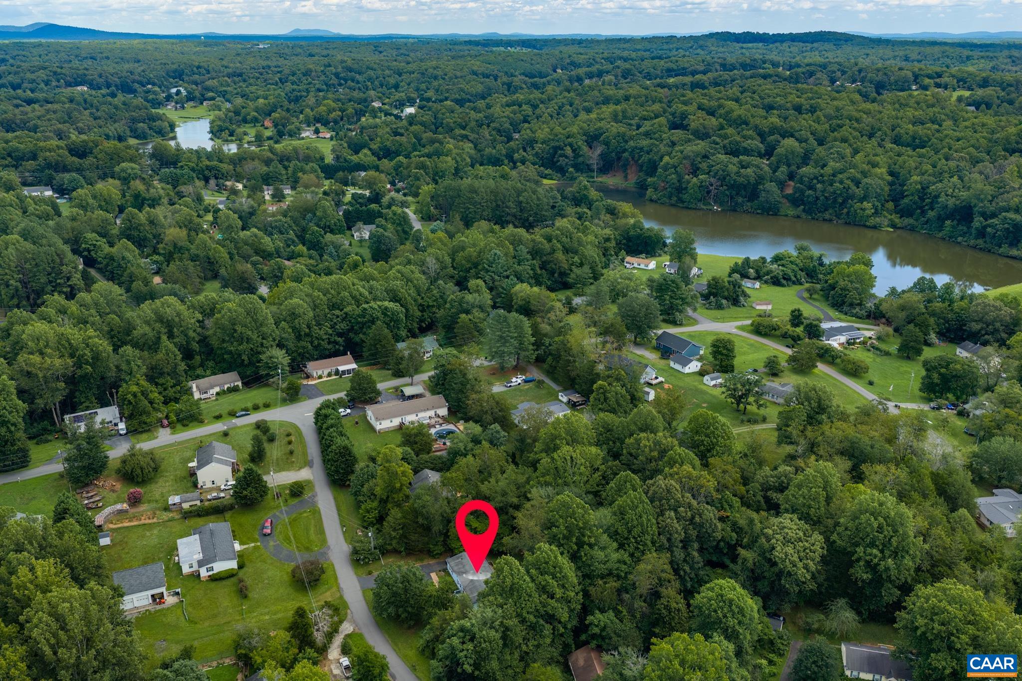 Breathtaking high-aerial landscape view highlighting the neighborhood's beautiful natural surroundings! Nestled amidst lush green rolling hills and mature canopy trees, this peaceful location features serene water views and idyllic countryside living.